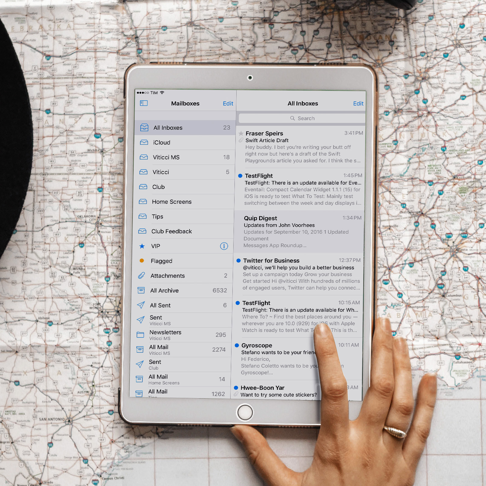 Schermo del tablet che mostra la posta in arrivo, sfondo della mappa. La mano tocca lo schermo.