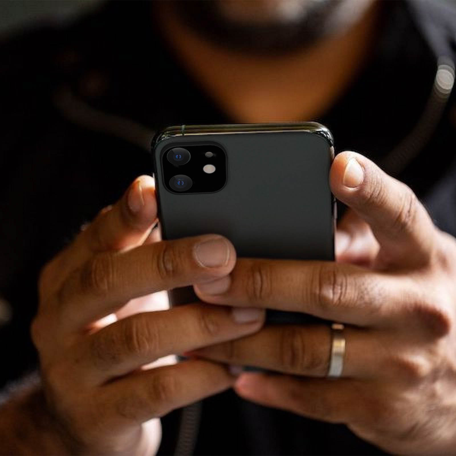 Una persona tiene in mano uno smartphone nero, mani visibili. Il telefono ha due obiettivi e un flash. Un anello d'argento al dito.