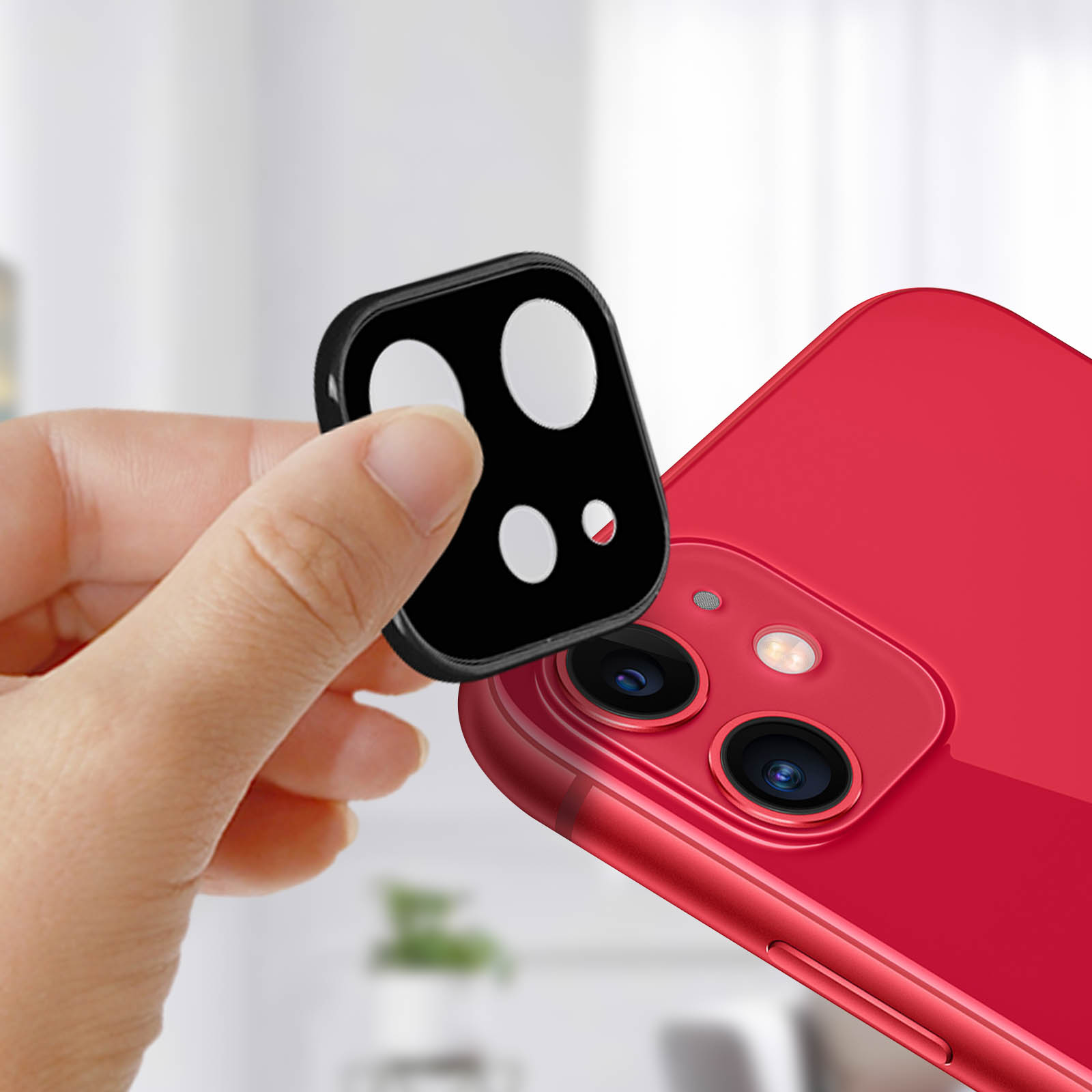 Una mano tiene un protettore per lenti nero sopra un telefono rosso con lenti della fotocamera. Lo sfondo è sfocato.