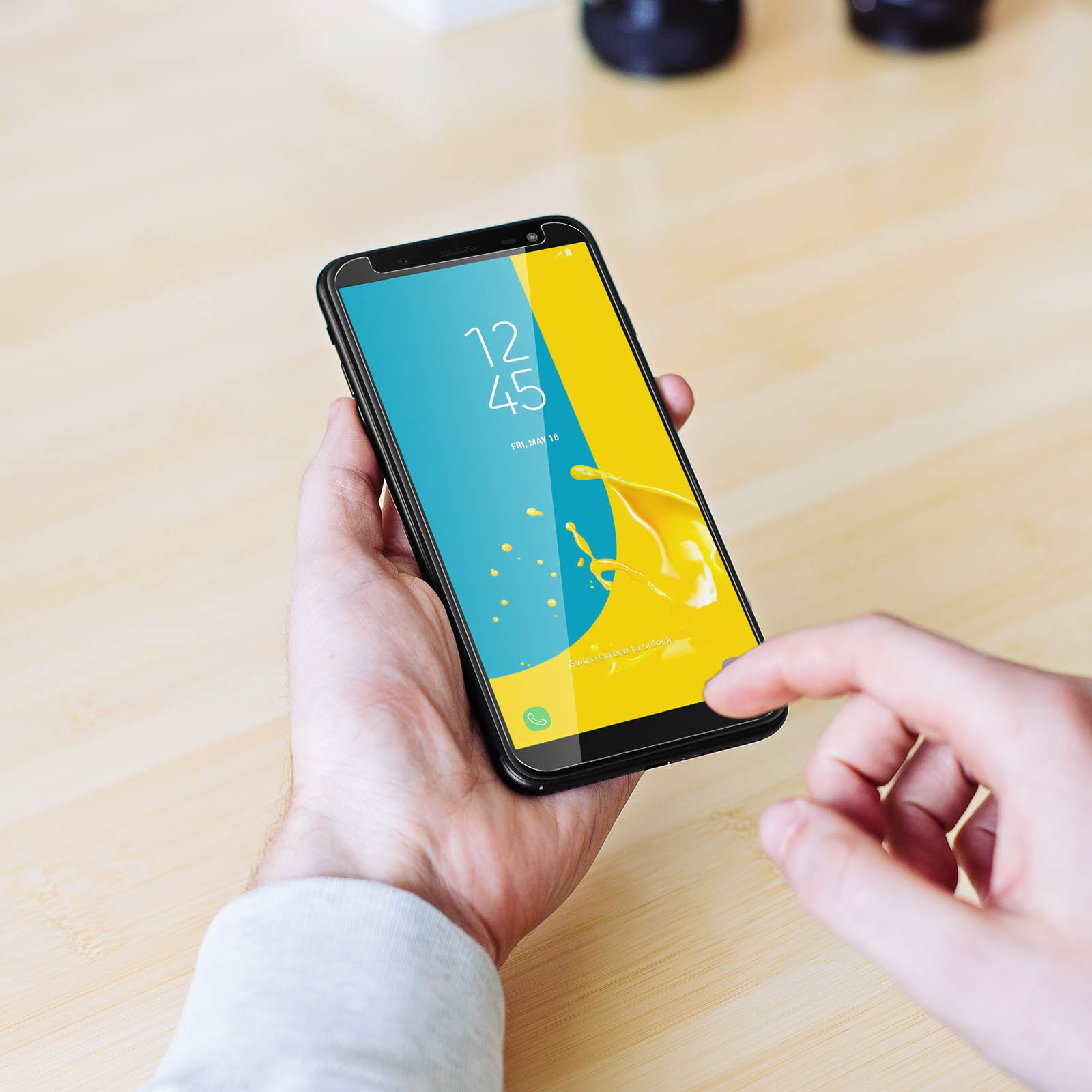 Una mano che tiene un telefono. Lo schermo mostra uno schizzo giallo e l'ora.