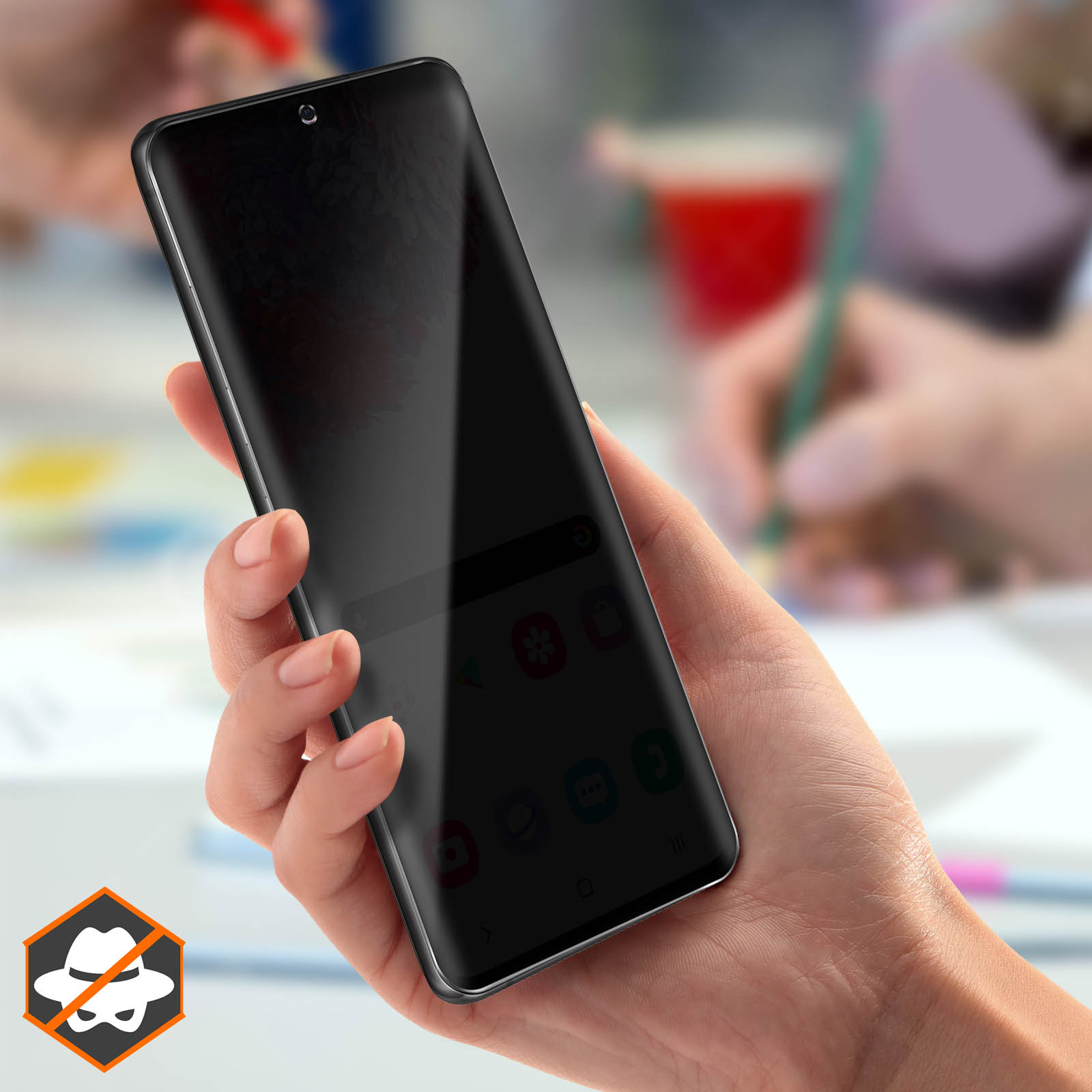 Una mano tiene in mano uno smartphone nero. Lo schermo è scuro. Altre mani sullo sfondo, una con una penna rossa.