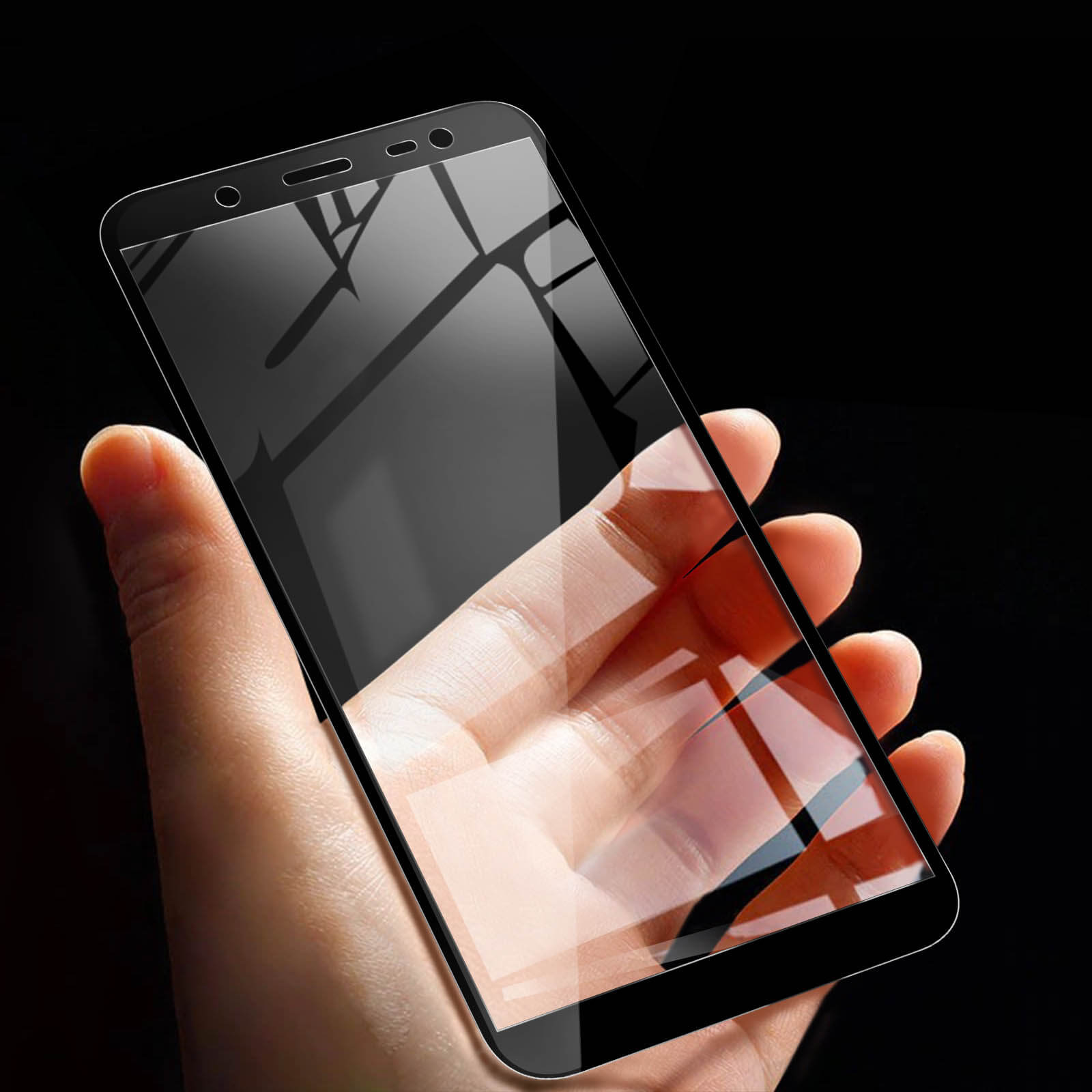 Una mano tiene uno smartphone con protezione schermo. Lo sfondo è nero. Lo schermo riflette l'ambiente.