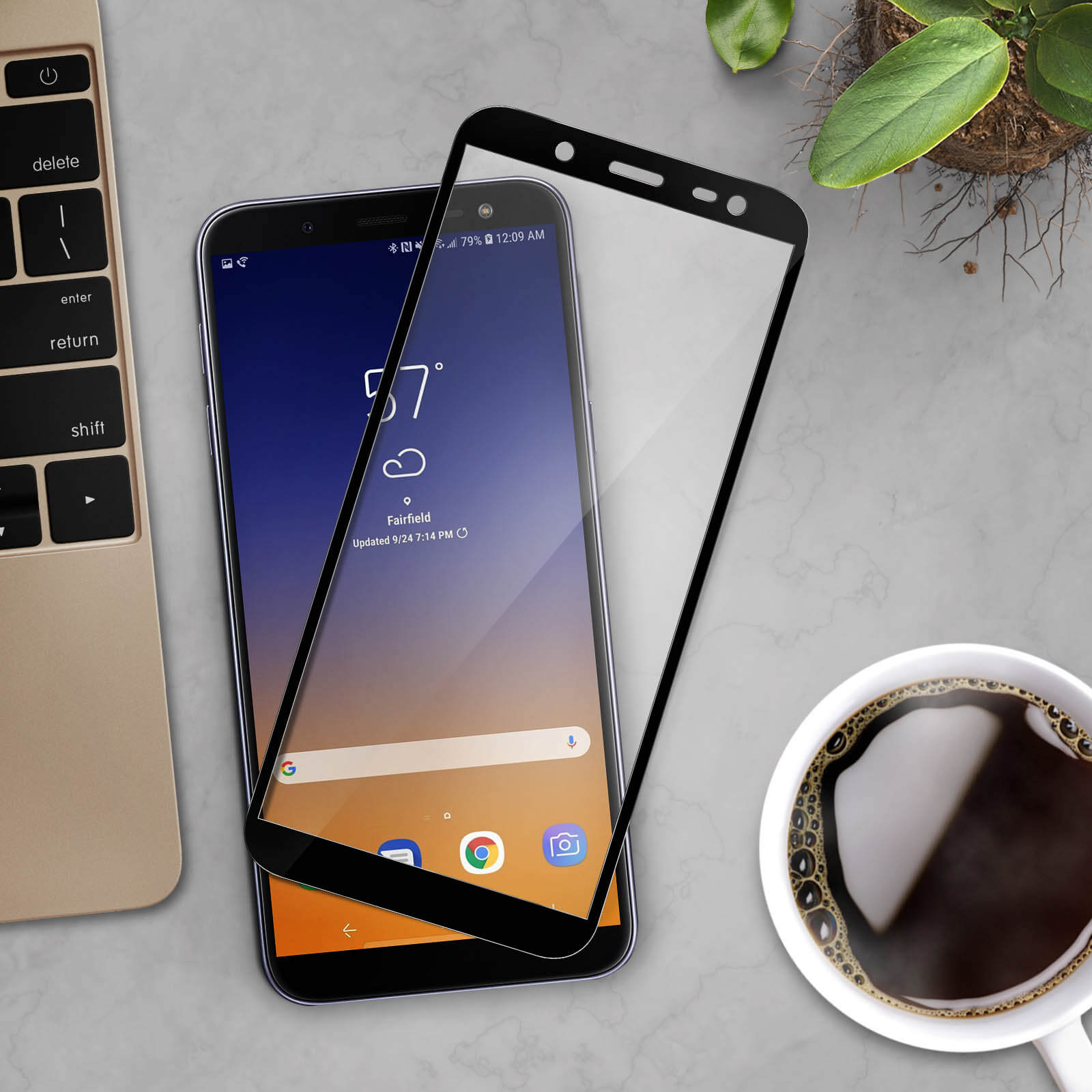 Uno smartphone con protezione schermo, un laptop e una tazza di caffè sono su una superficie di marmo. Si vede una piccola pianta.
