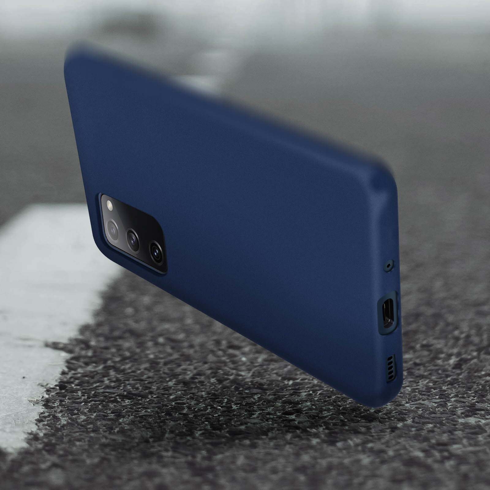 Custodia per telefono blu scuro che fluttua in aria, contro uno sfondo di asfalto strutturato.