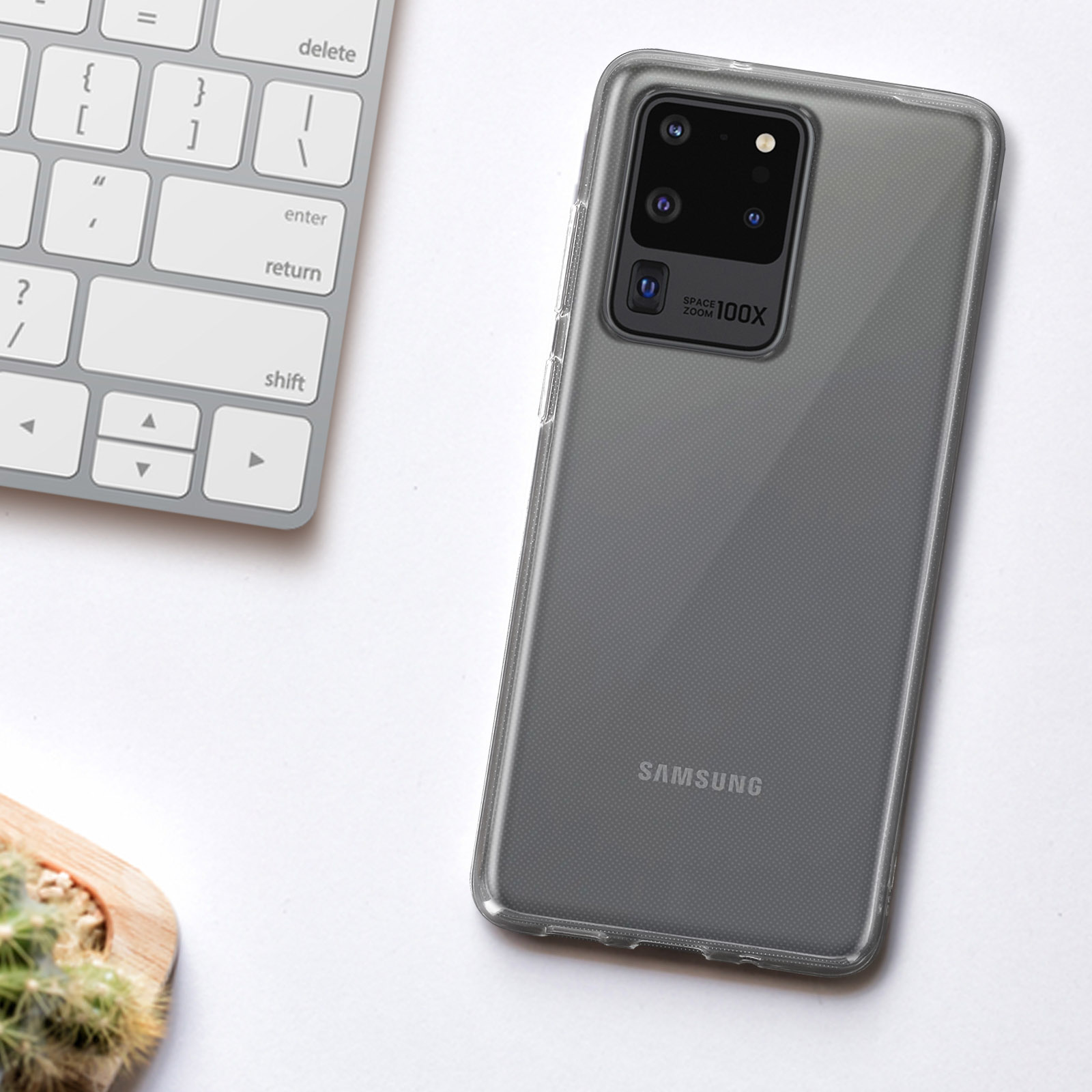 Un telefono in una custodia trasparente è vicino a una tastiera. Il telefono è grigio. La custodia è trasparente.