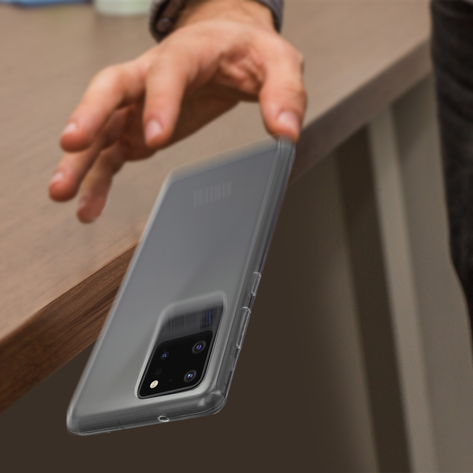 Una mano che afferra un telefono in una custodia trasparente su un tavolo di legno.