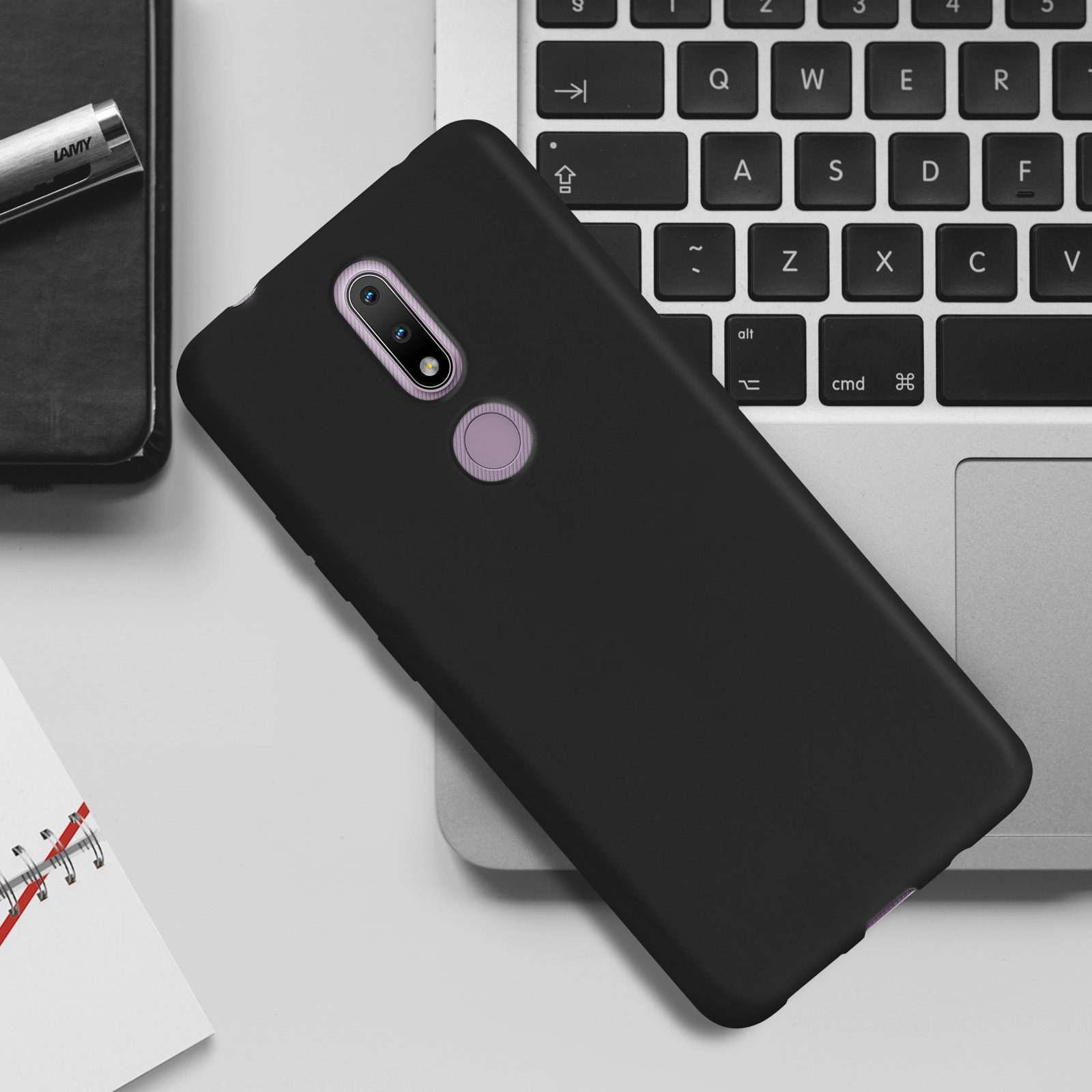 Custodia nera per telefono su tastiera portatile. Penna e taccuino sullo sfondo.