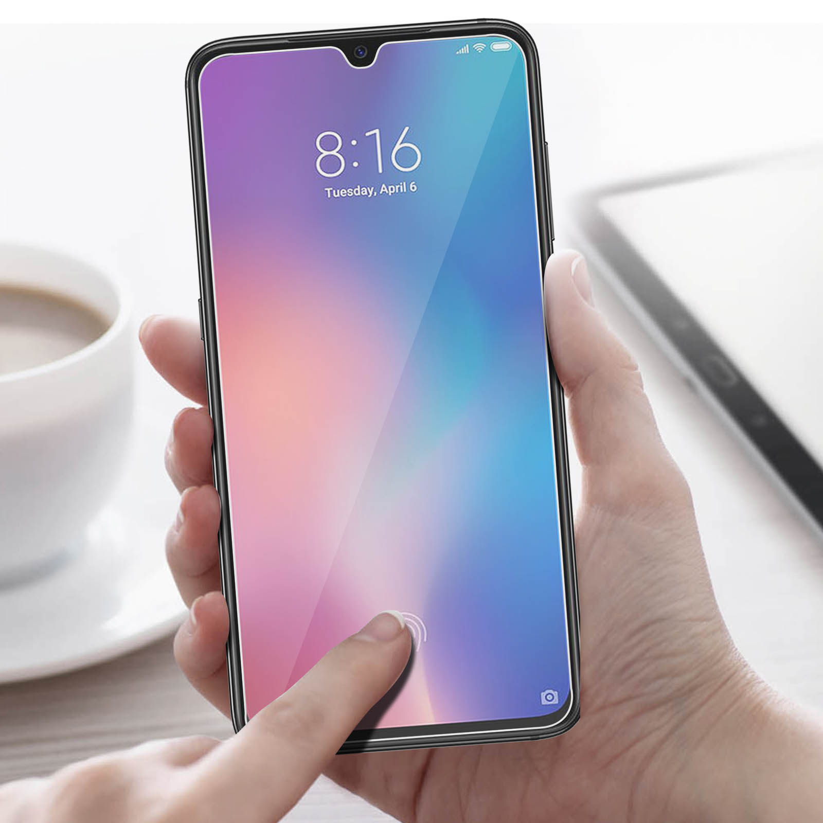 Mano che tocca lo schermo del telefono che mostra ora e data. Una tazza di caffè è sullo sfondo sfocato.