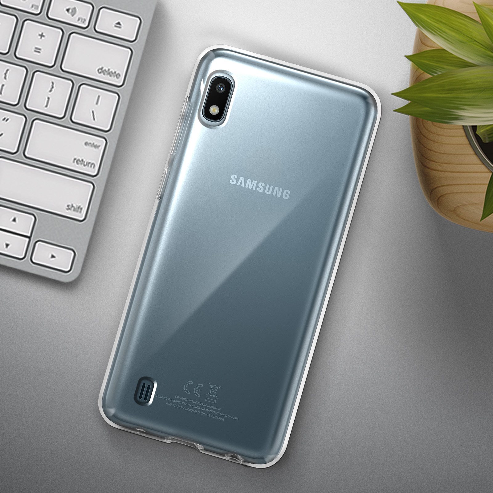 Telefono Samsung argento in una custodia trasparente, con tastiera e pianta sullo sfondo.