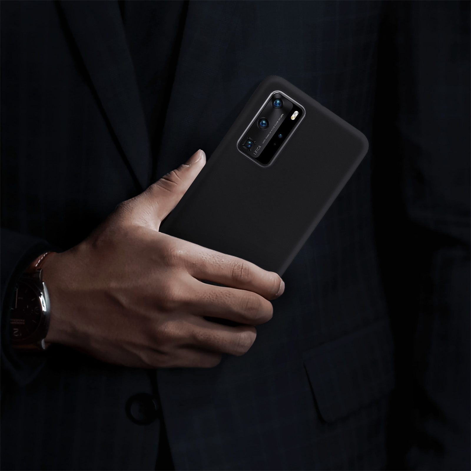 Una mano tiene un telefono nero. Il telefono ha più fotocamere. L'uomo indossa un abito.