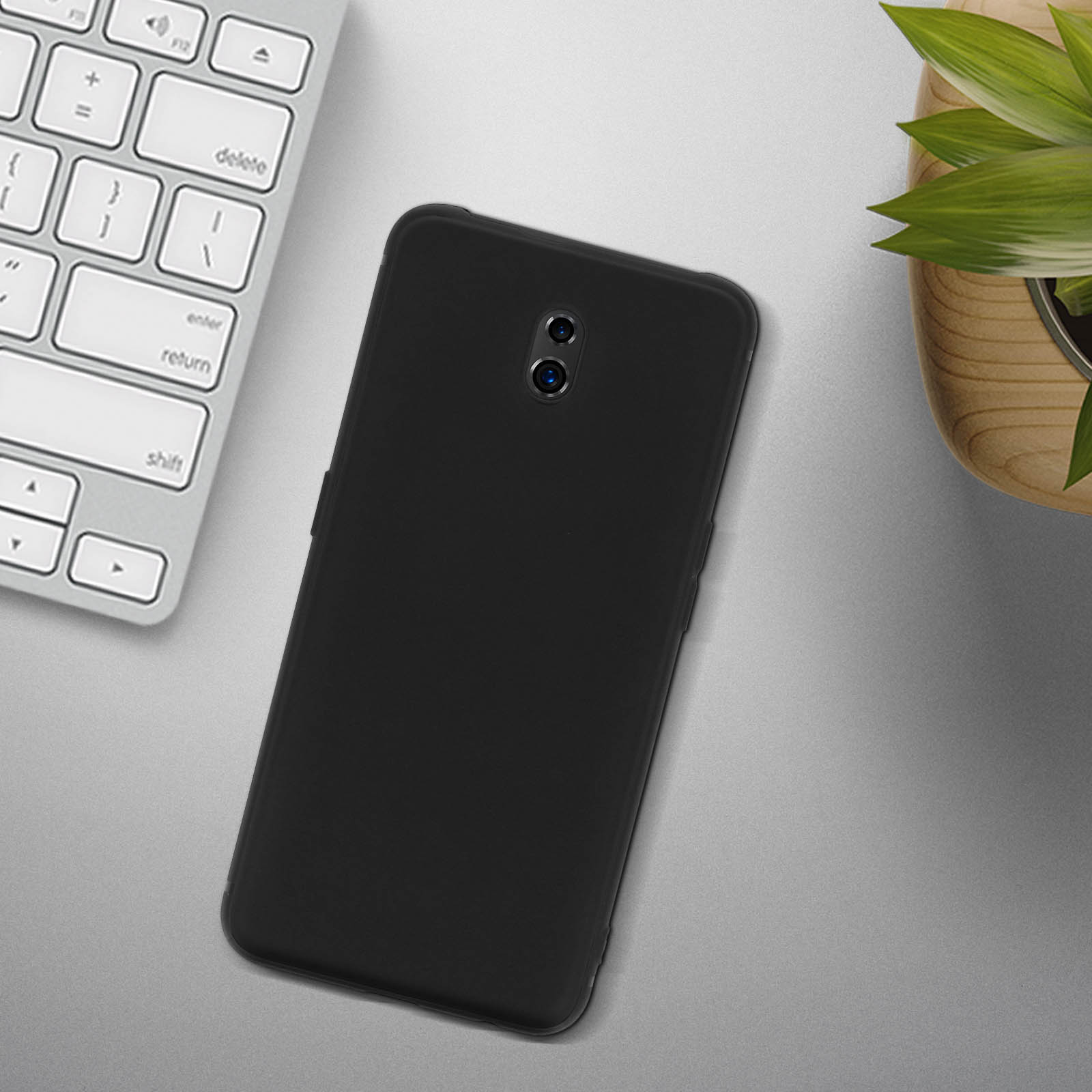Schwarzes Telefon mit Dual-Kamera liegt auf grauer Oberfläche neben Tastatur und Pflanze.