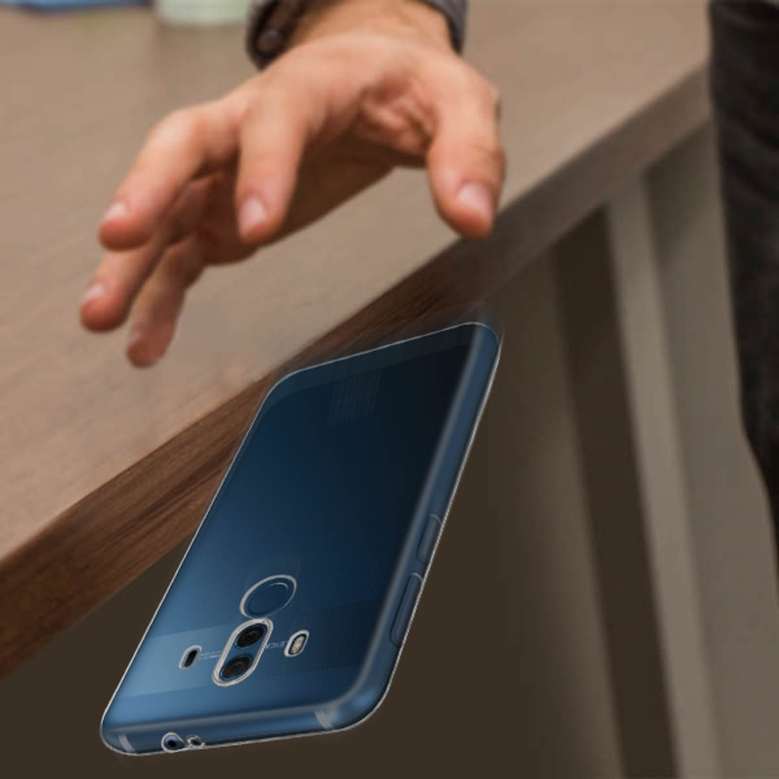 Una mano che si allunga verso un telefono che cade da un tavolo. Il telefono è blu e ha una custodia trasparente.