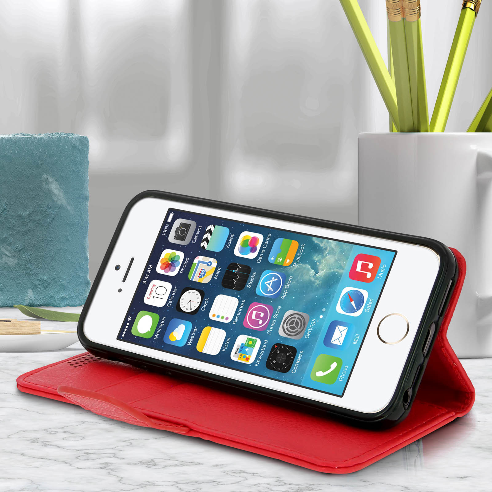 Un telefono bianco in una custodia di pelle rossa su un tavolo. Una tazza bianca e delle matite sullo sfondo.