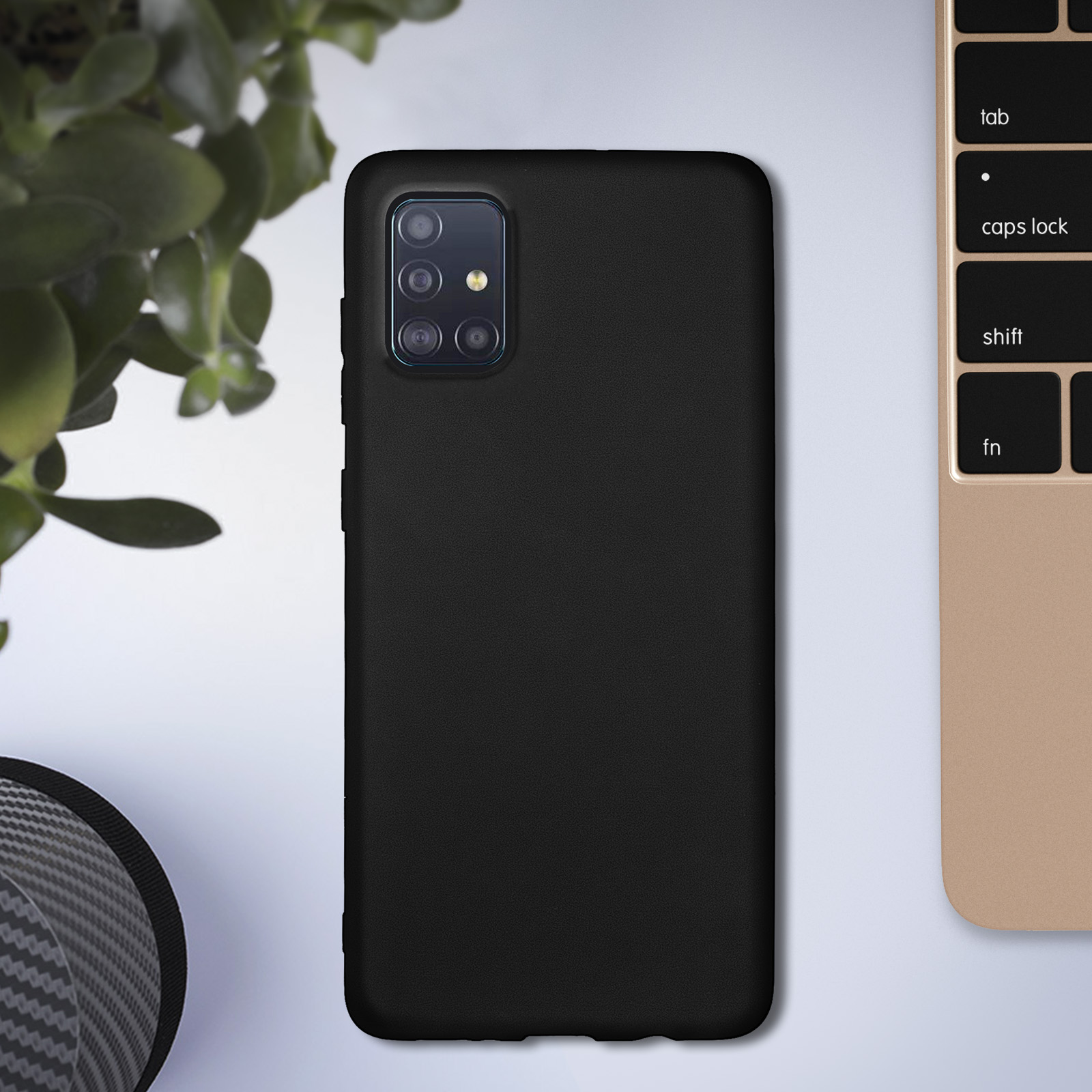 Coque de téléphone noire sur une surface blanche, avec une plante verte et un clavier en arrière-plan.