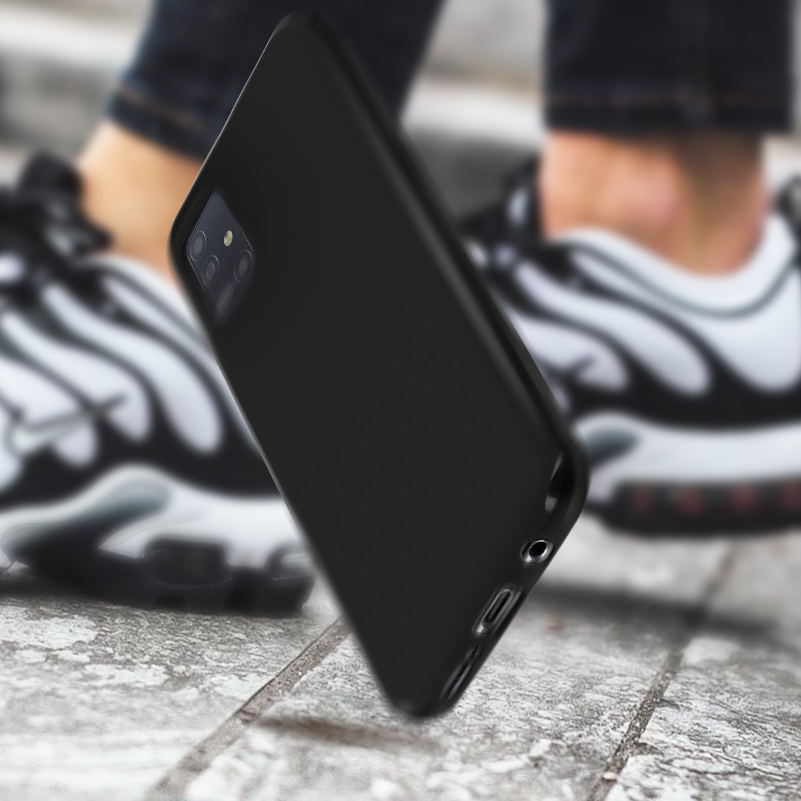 Coque de téléphone noire sur un fond, avec des pieds à l'arrière. Arrière-plan flou.