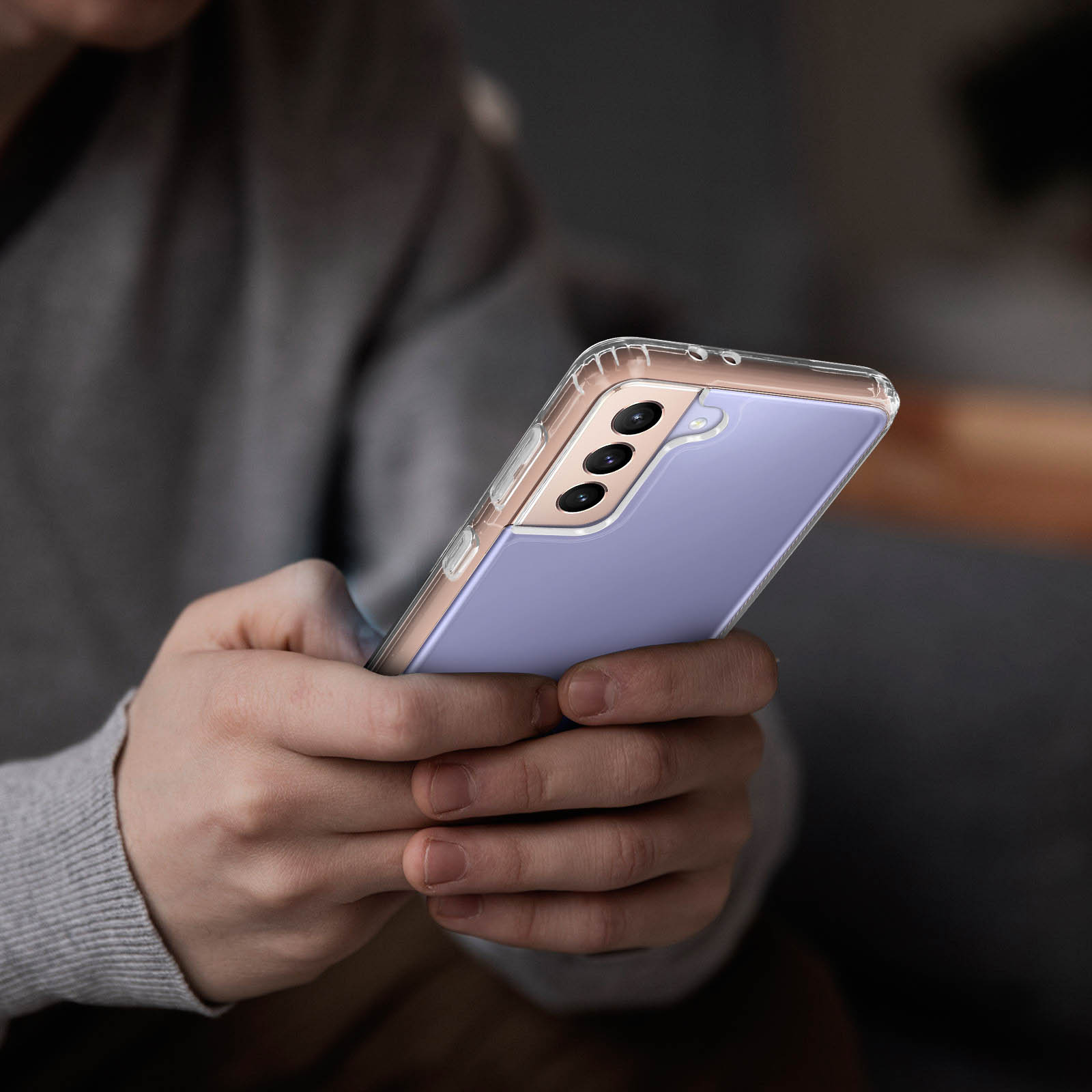Persona che tiene un telefono lavanda in una custodia trasparente. Sfondo sfocato.