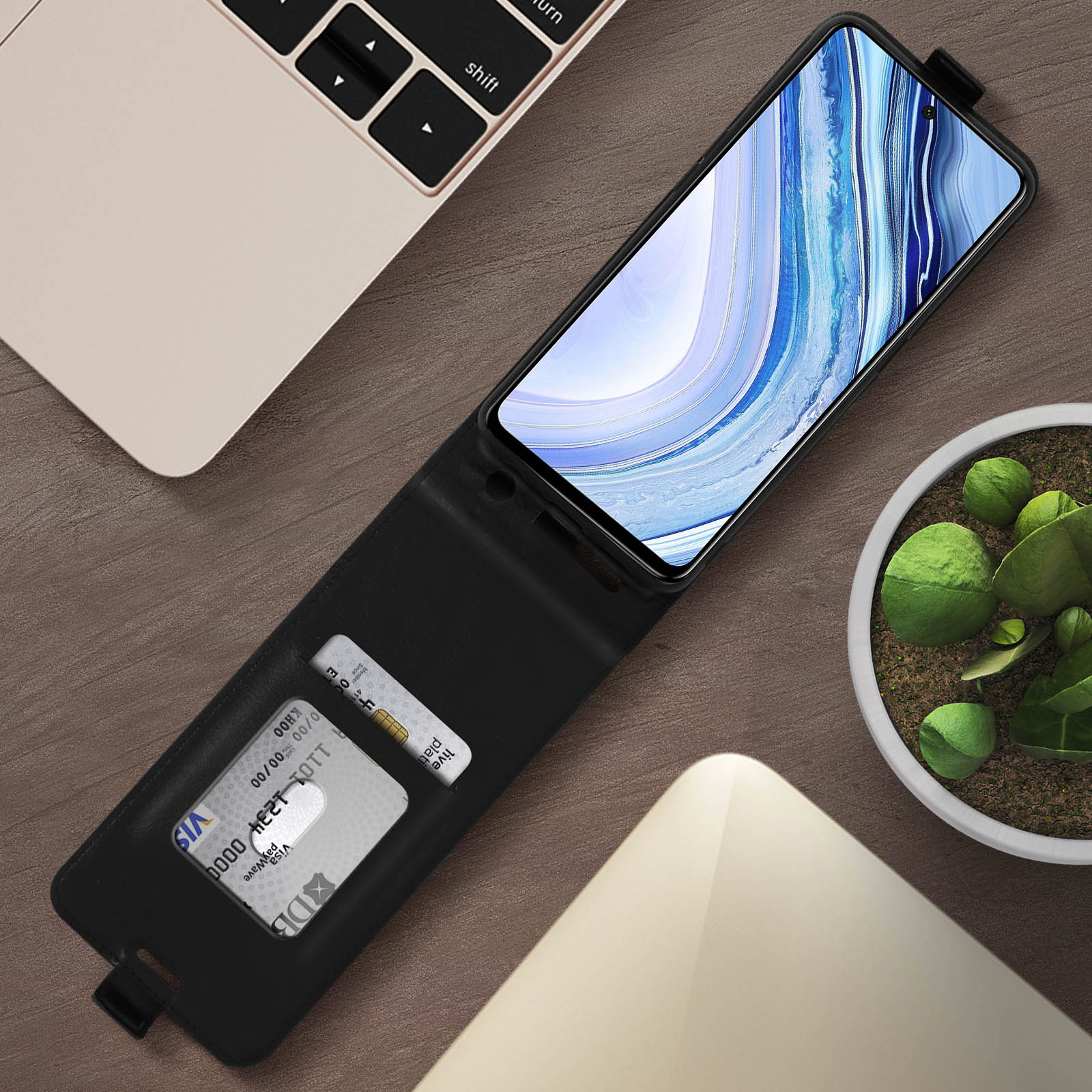 Un étui de téléphone ouvert, avec une carte de crédit à l'intérieur. Un ordinateur portable en arrière-plan.