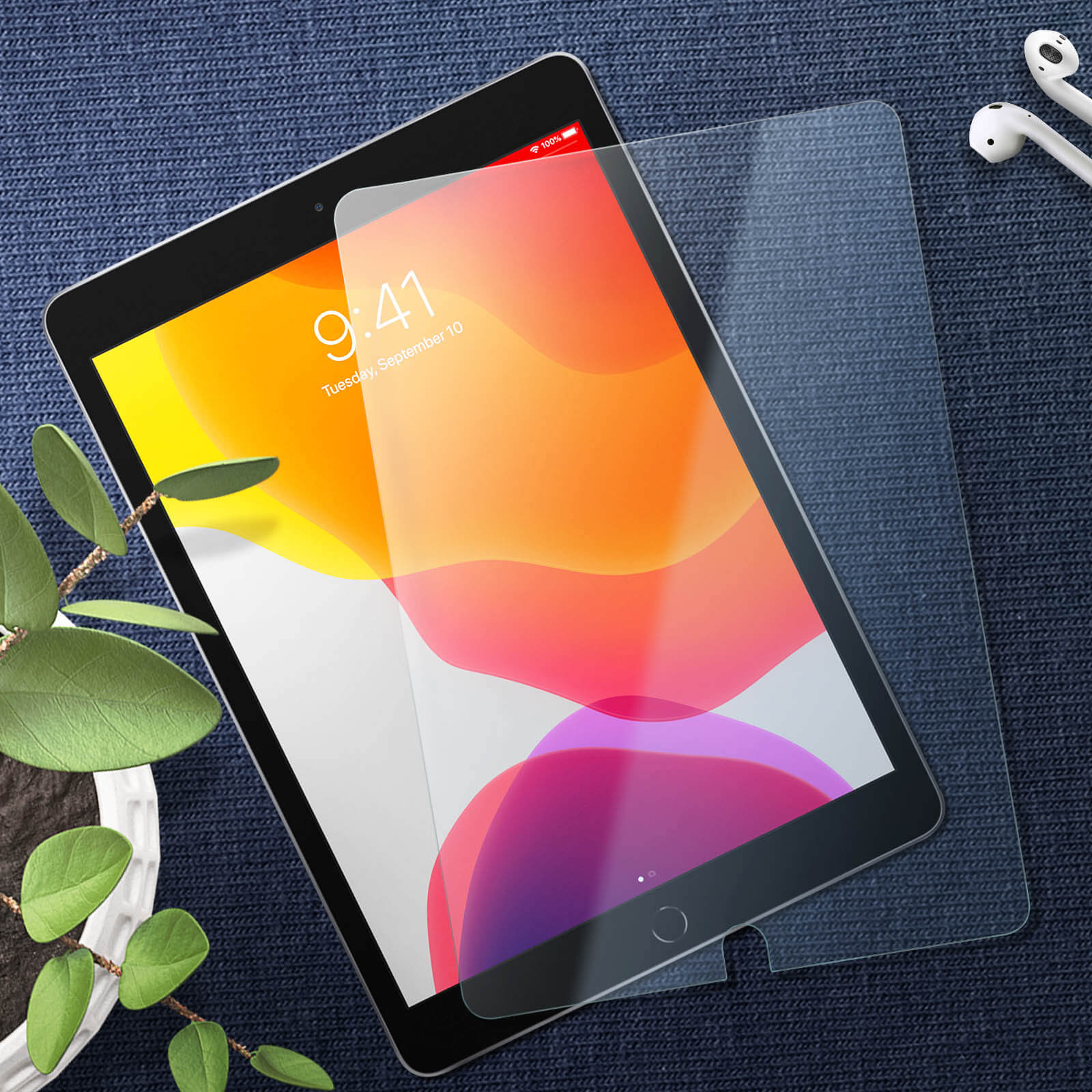 Un iPad con protezione schermo è su una superficie strutturata con auricolari e una pianta.