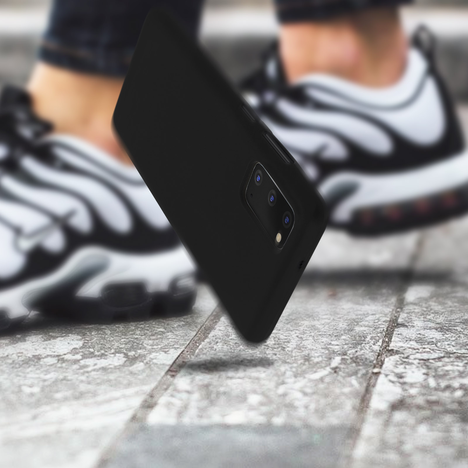 Une coque de téléphone noire, tombant. La coque a plusieurs ouvertures pour l'appareil photo. Le fond est une surface en béton.