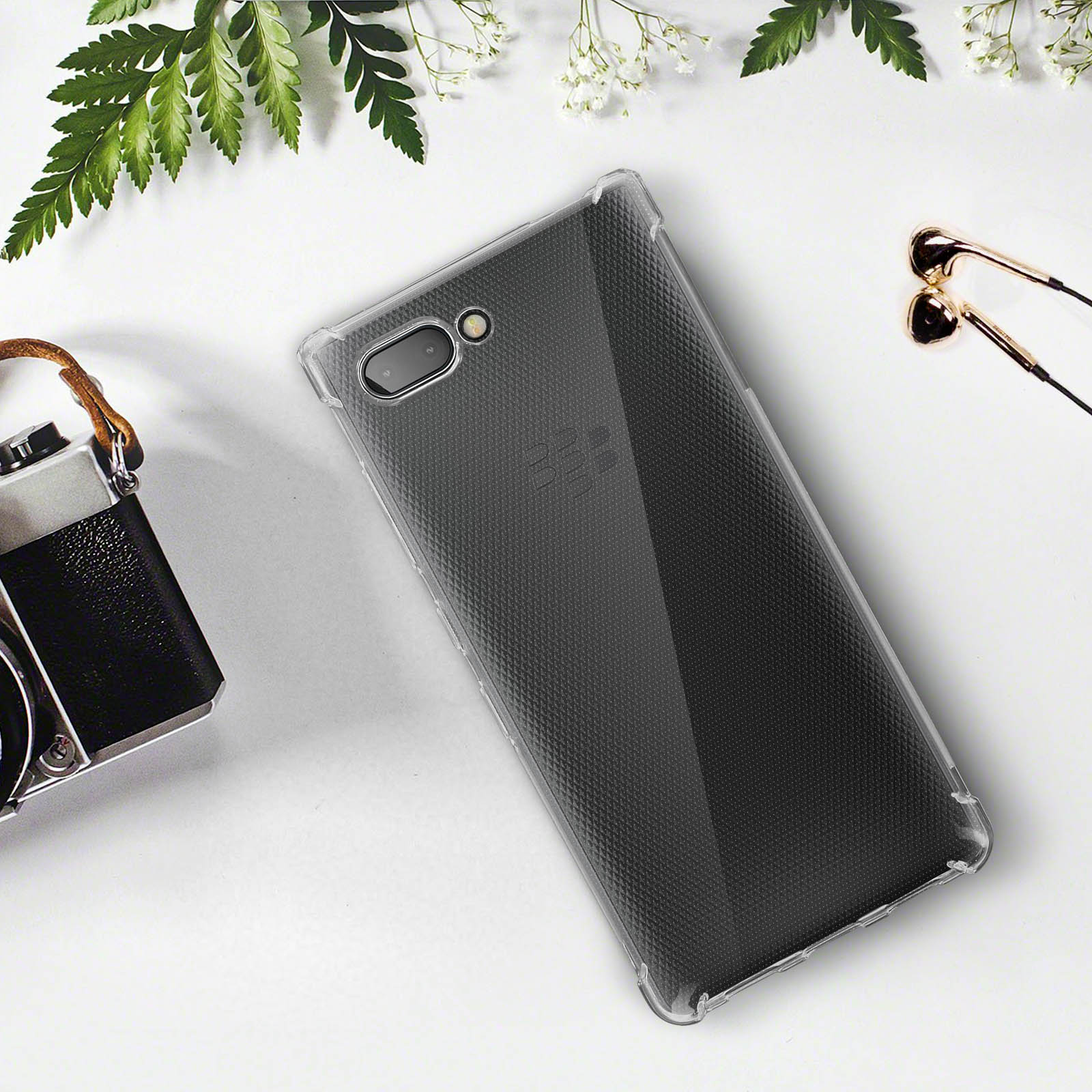 Custodia trasparente per telefono su superficie bianca con fotocamera, foglie e cuffie.