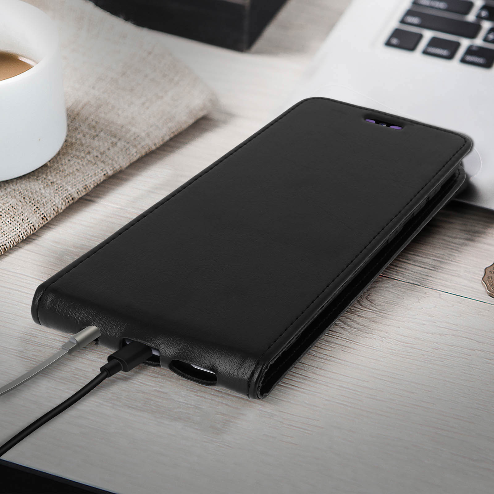 Étui de téléphone en cuir noir ouvert. Câble de chargement à l'intérieur. Ordinateur portable sur une surface en bois.