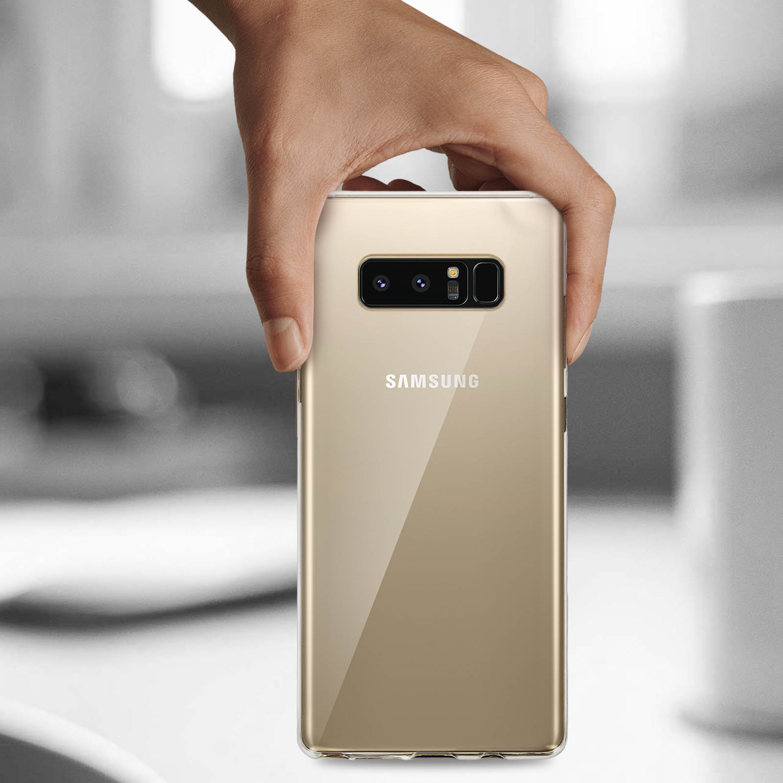 Una mano tiene una custodia dorata con retro trasparente. Il telefono è un Samsung.