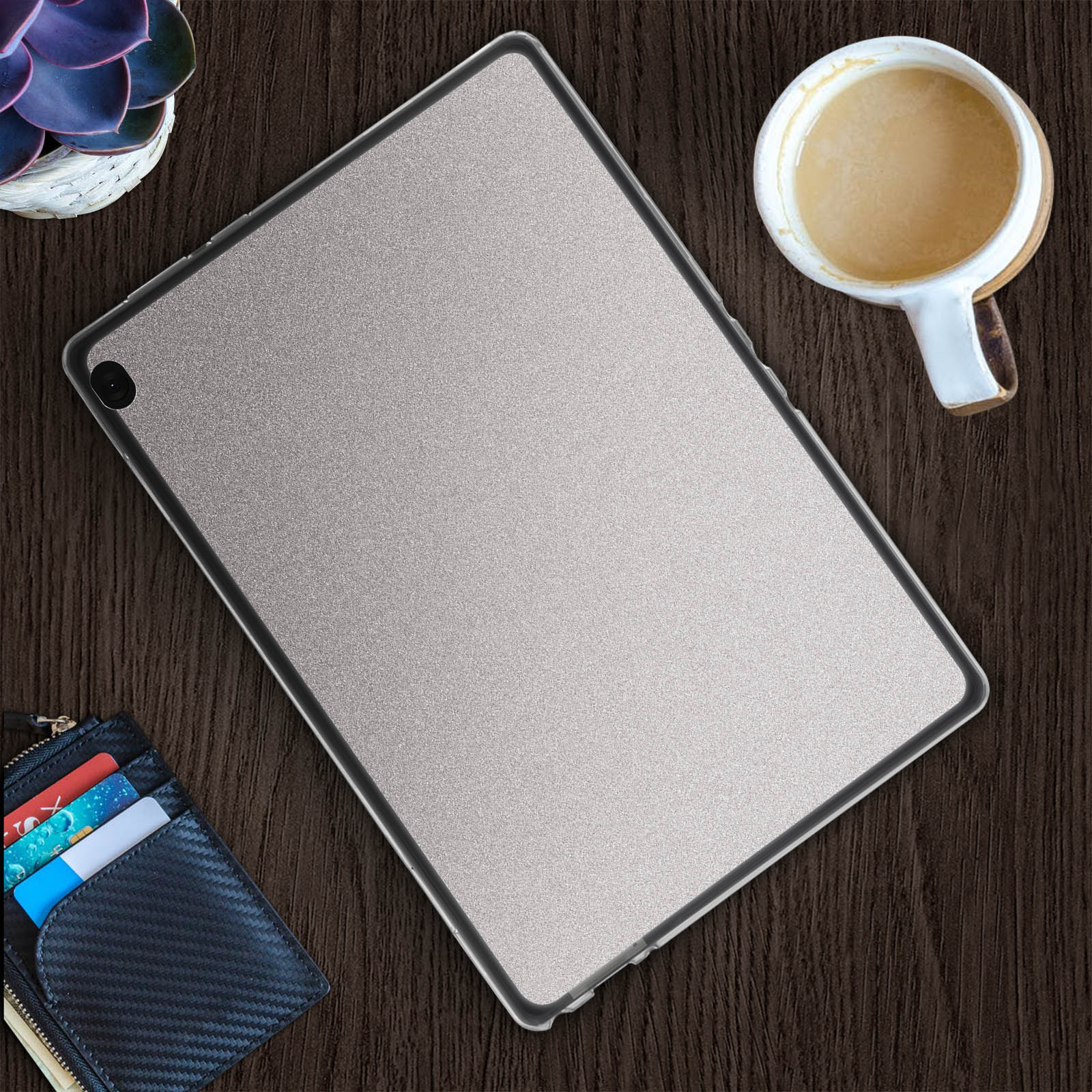 Ein Tablet in einer durchsichtigen Hülle, neben einer Kaffeetasse, einer Geldbörse und einer kleinen Pflanze.