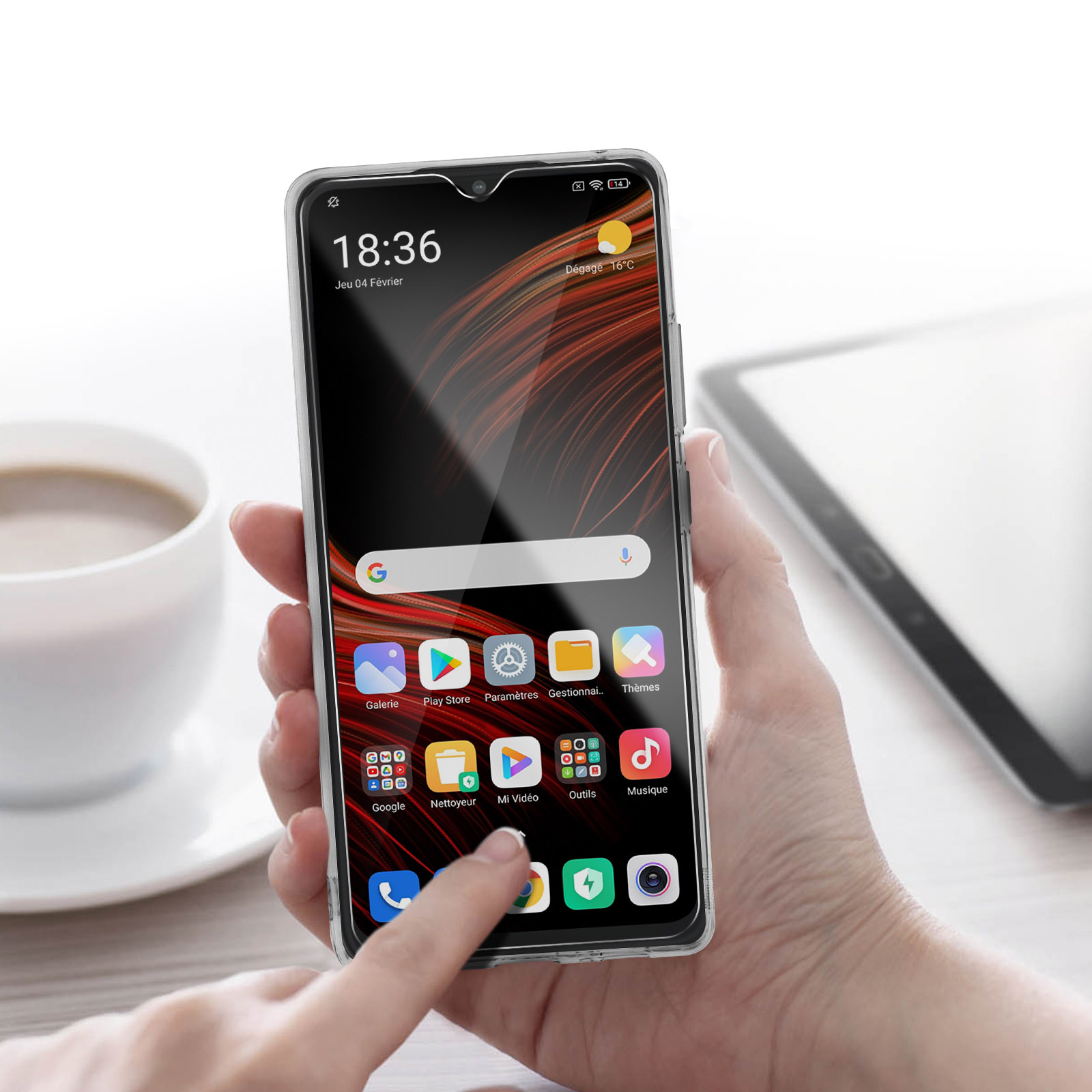 Una mano che tiene un telefono con app sullo schermo. Una tazza di caffè, un tablet e uno sfondo sfocato sono visibili.