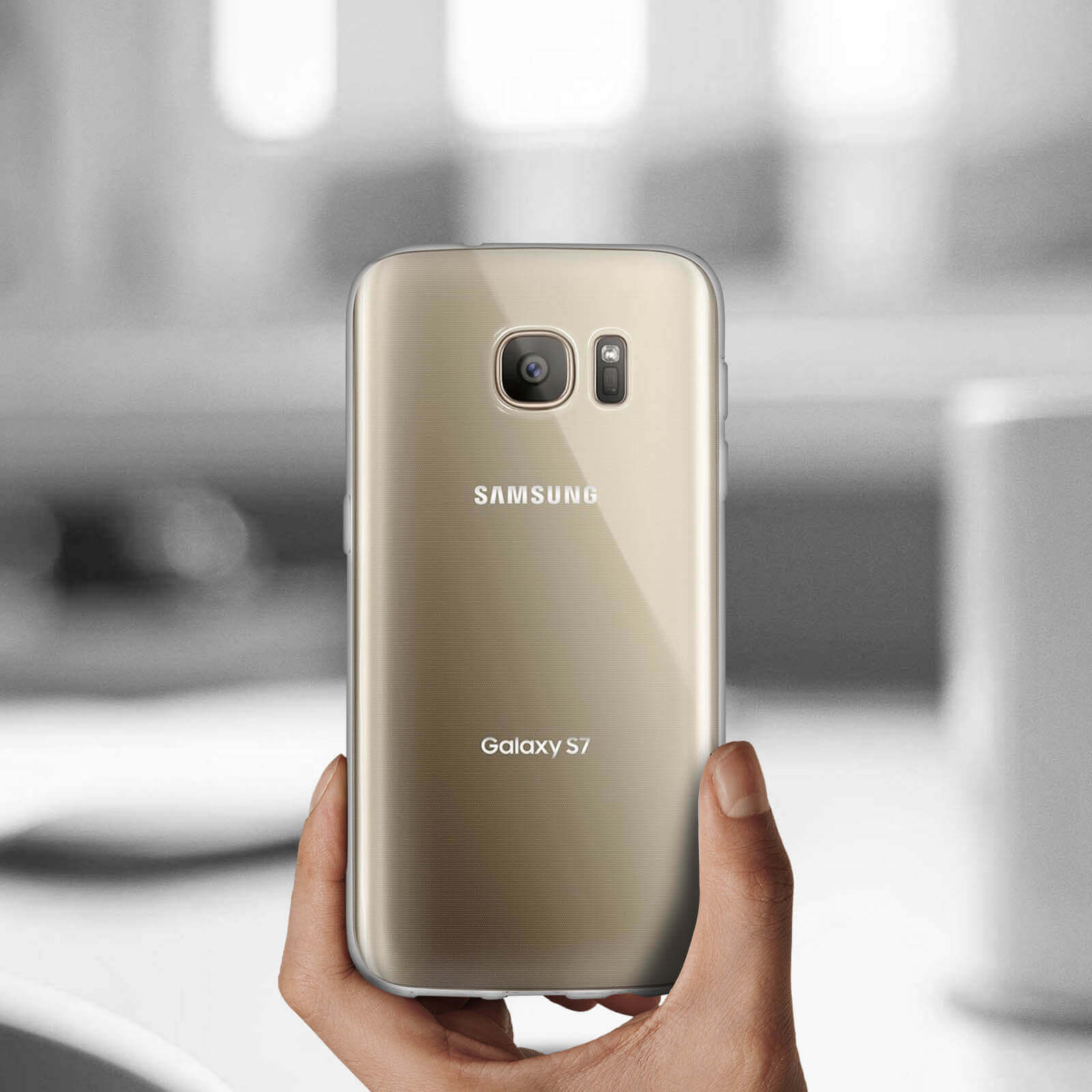 Mano che tiene un telefono Samsung Galaxy S7 dorato in una custodia trasparente. Sfondo sfocato.