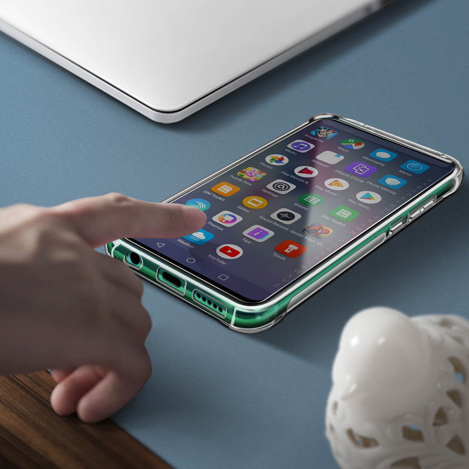 Una mano tocca un telefono con una custodia trasparente, appoggiato su una superficie blu.