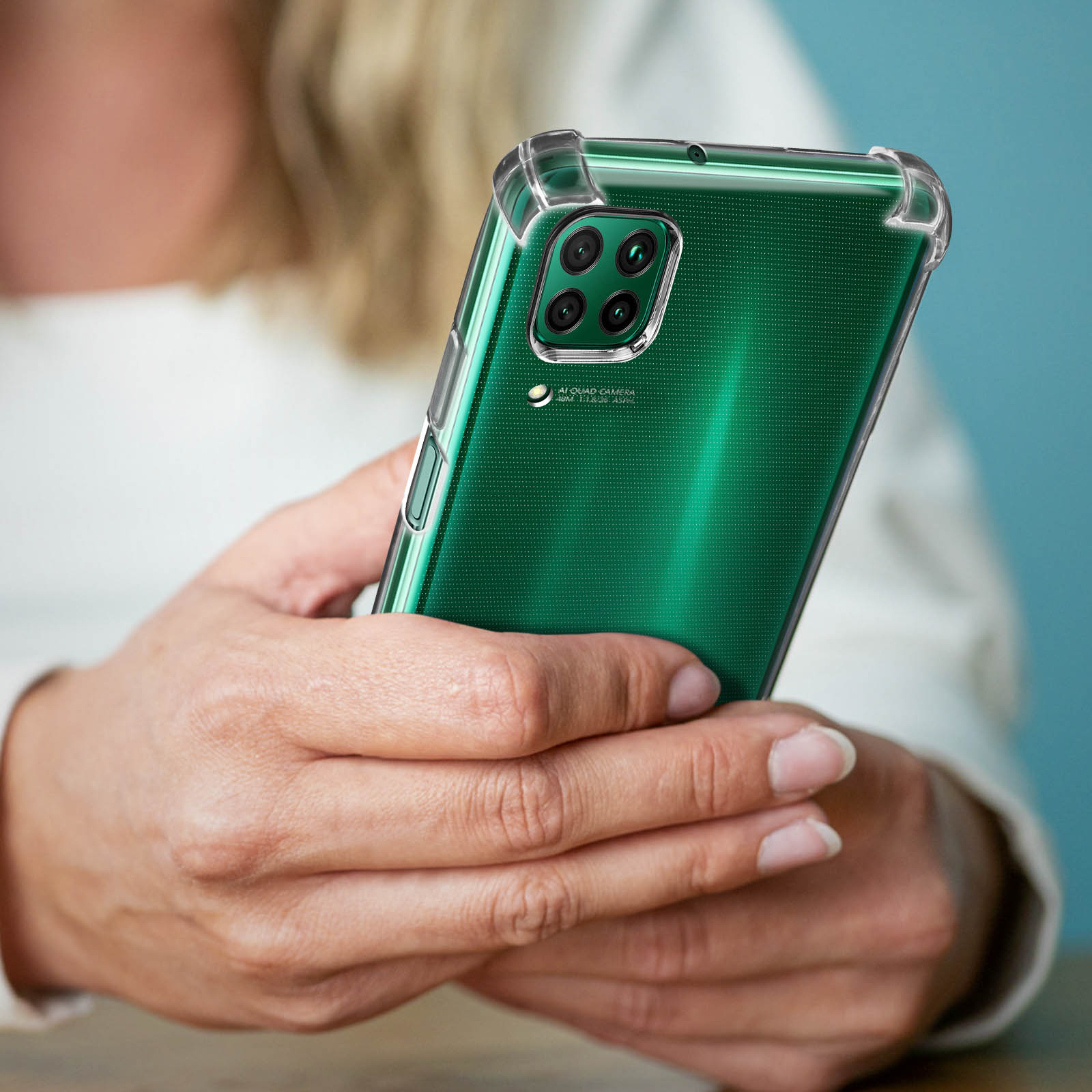Una persona tiene in mano un telefono verde con una custodia trasparente, su uno sfondo azzurro.