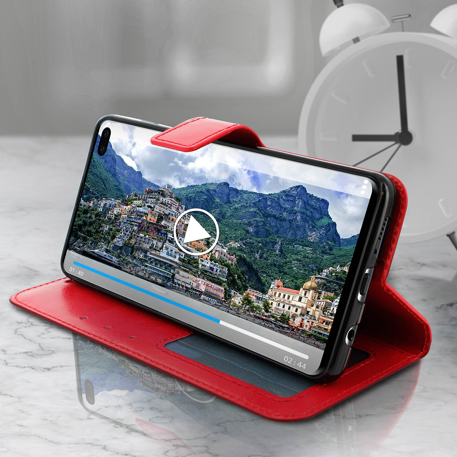 Telefono in custodia rossa, mostra un video in riproduzione. Una sveglia bianca sullo sfondo.