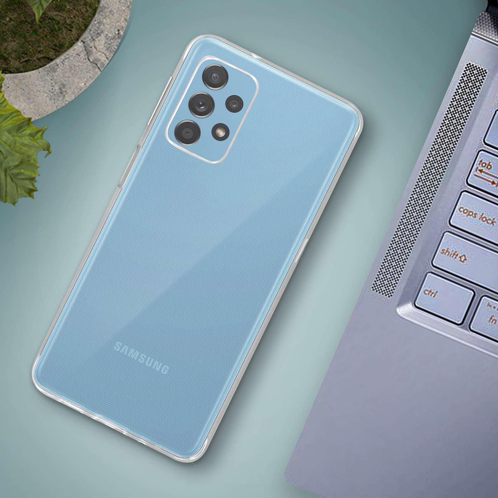 Un telefono azzurro con custodia trasparente su una scrivania con un laptop. Sfondo sfocato.