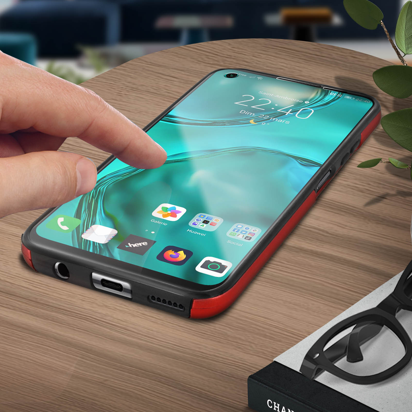 Een hand raakt een telefoon aan die pictogrammen weergeeft op een houten tafel, met een bril en een boek.