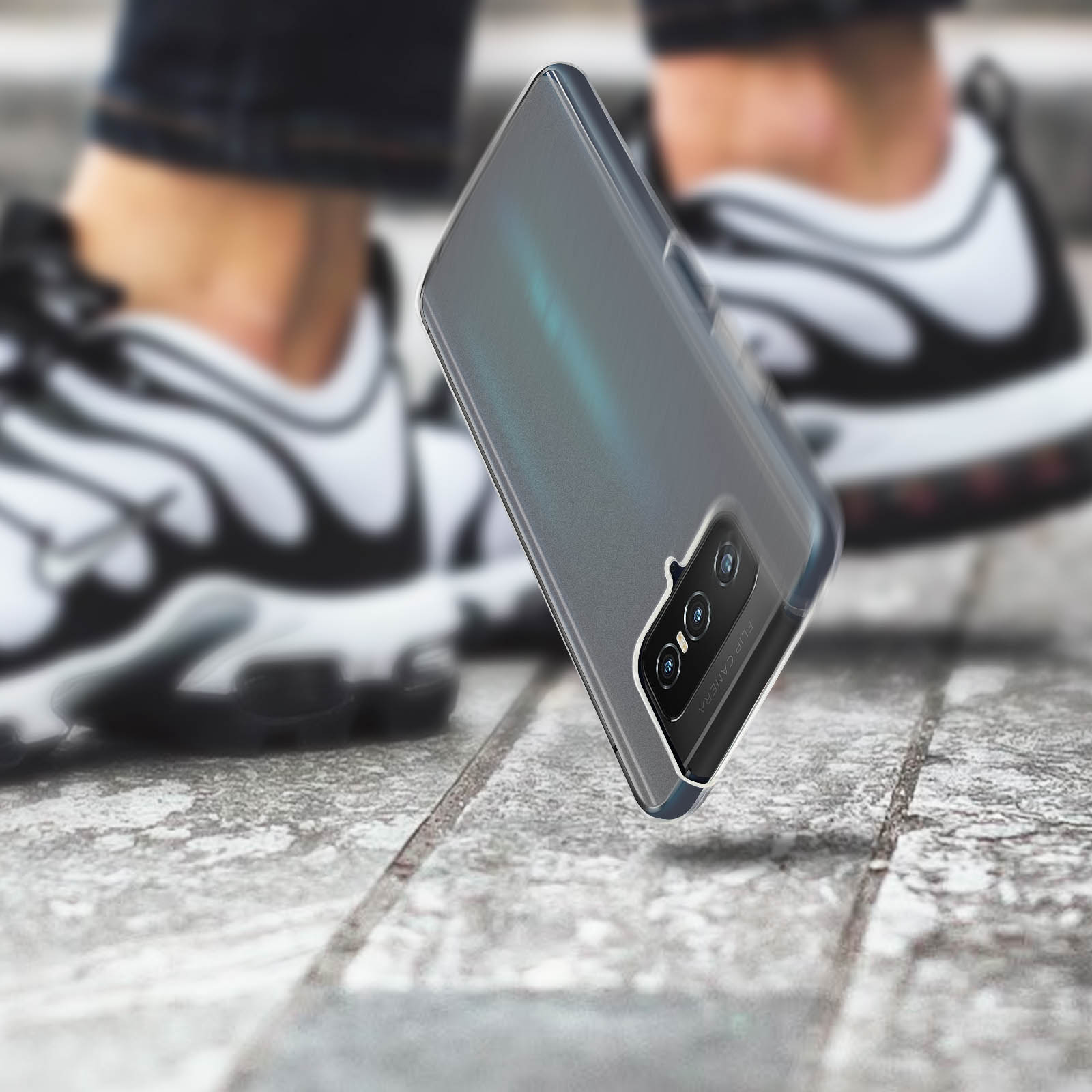 Una custodia grigia per telefono che cade. Sneakers sfocate sullo sfondo, su una superficie grigia.