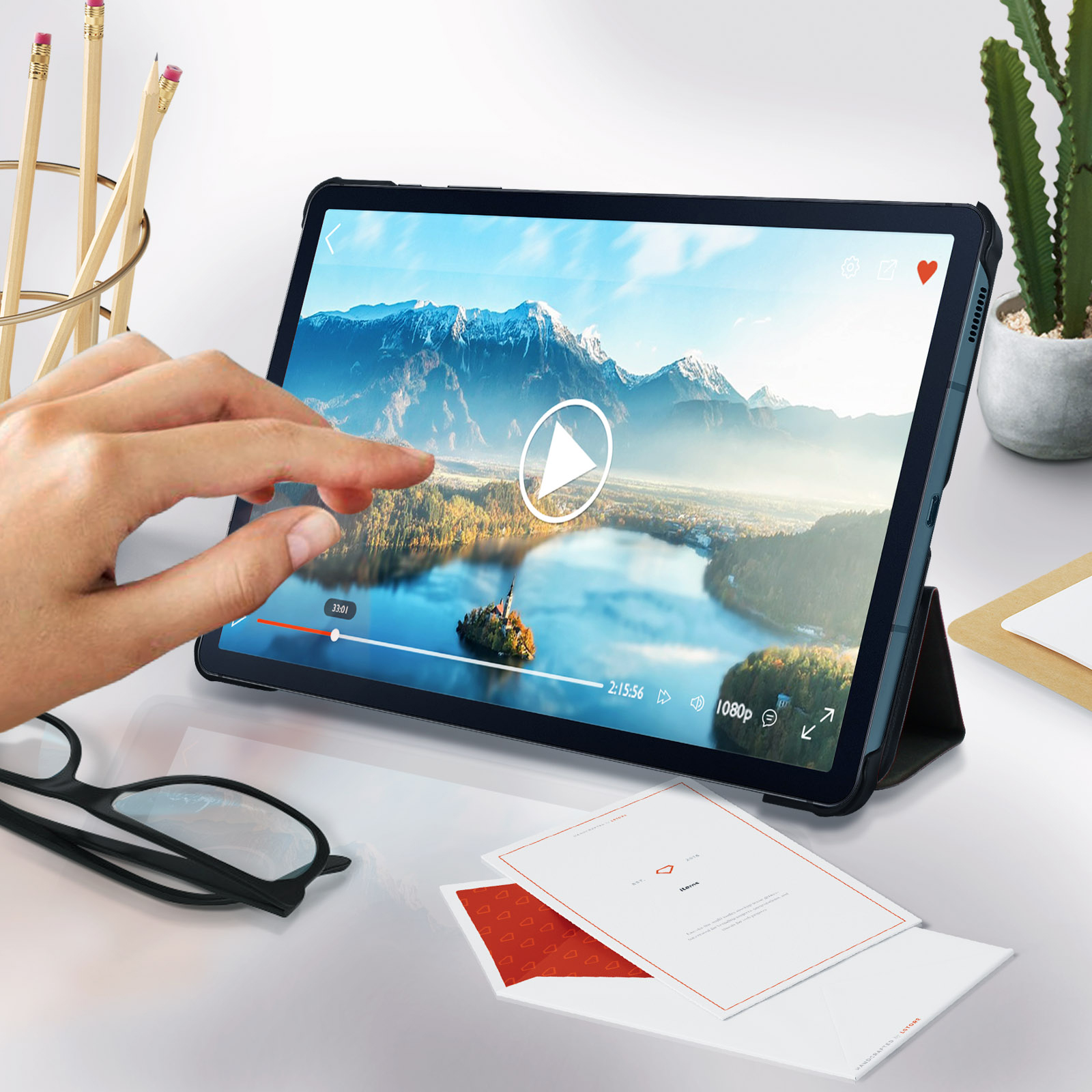 Tablet con schermo su un tavolo. Una mano tocca lo schermo. Penne e occhiali sullo sfondo.