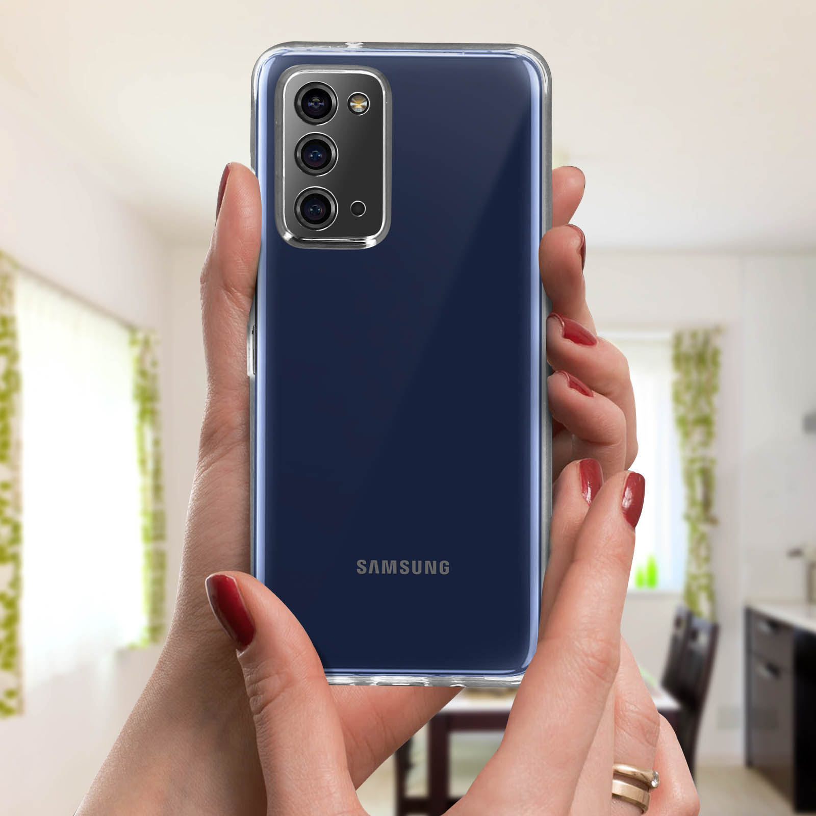 Handen houden een telefoon met een blauwe achterkant vast. De achtergrond is een wazige keuken.