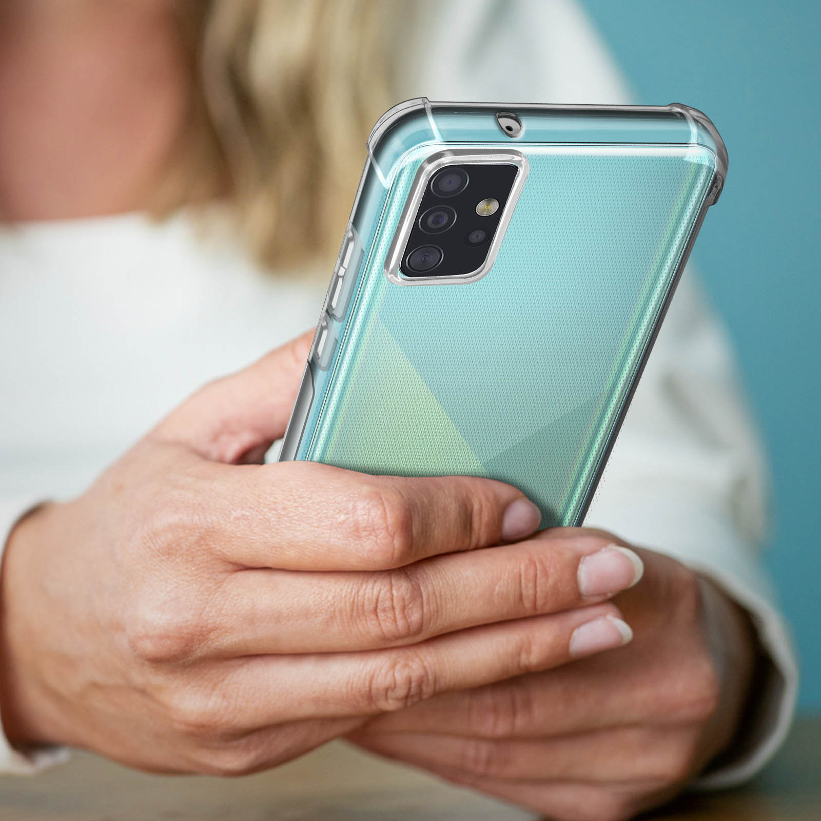 Le mani tengono un telefono verde acqua con una custodia trasparente. Il telefono ha tre fotocamere sul retro.