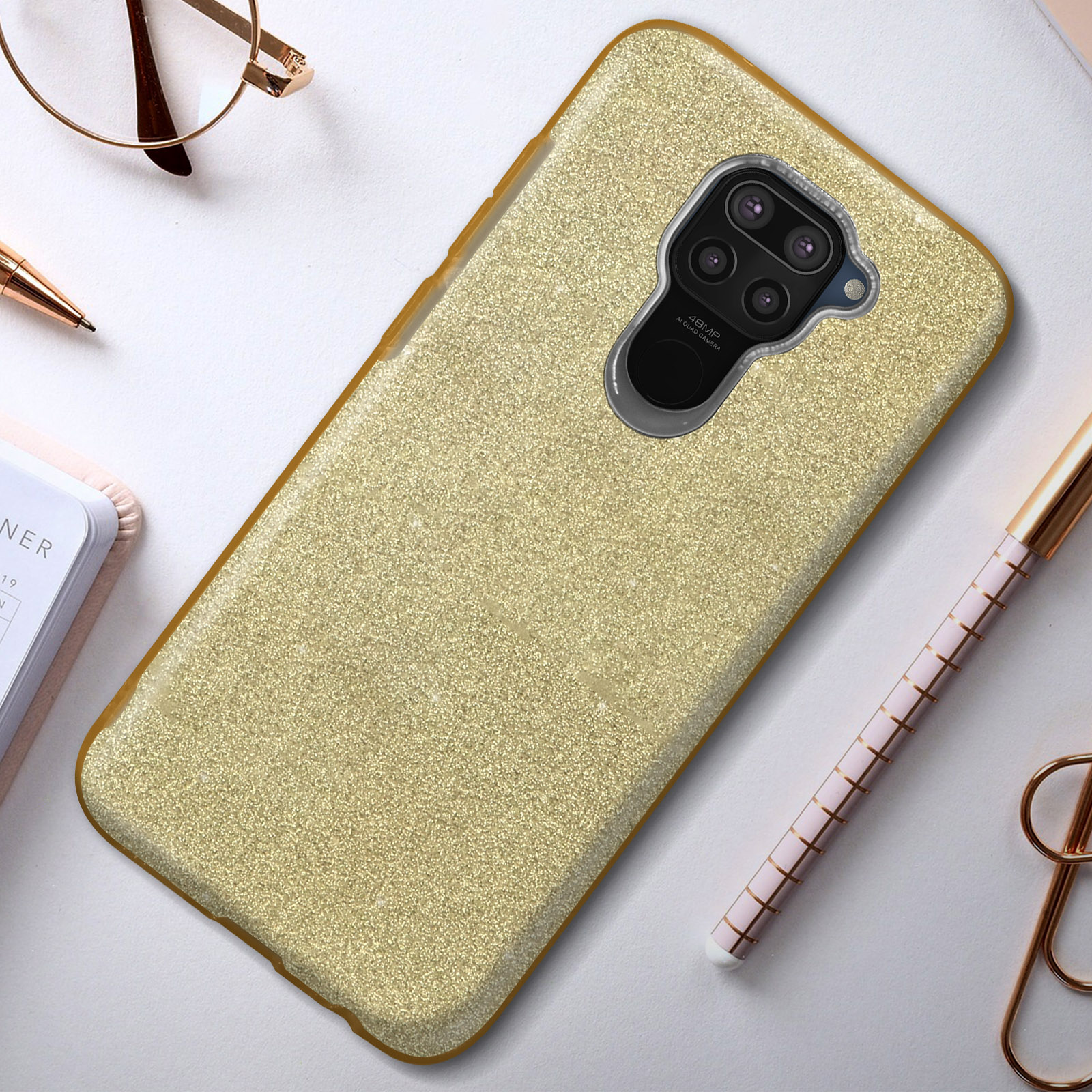 Een gouden glitter telefoonhoesje met een uitsparing voor de cameralens, op een bureau met items.