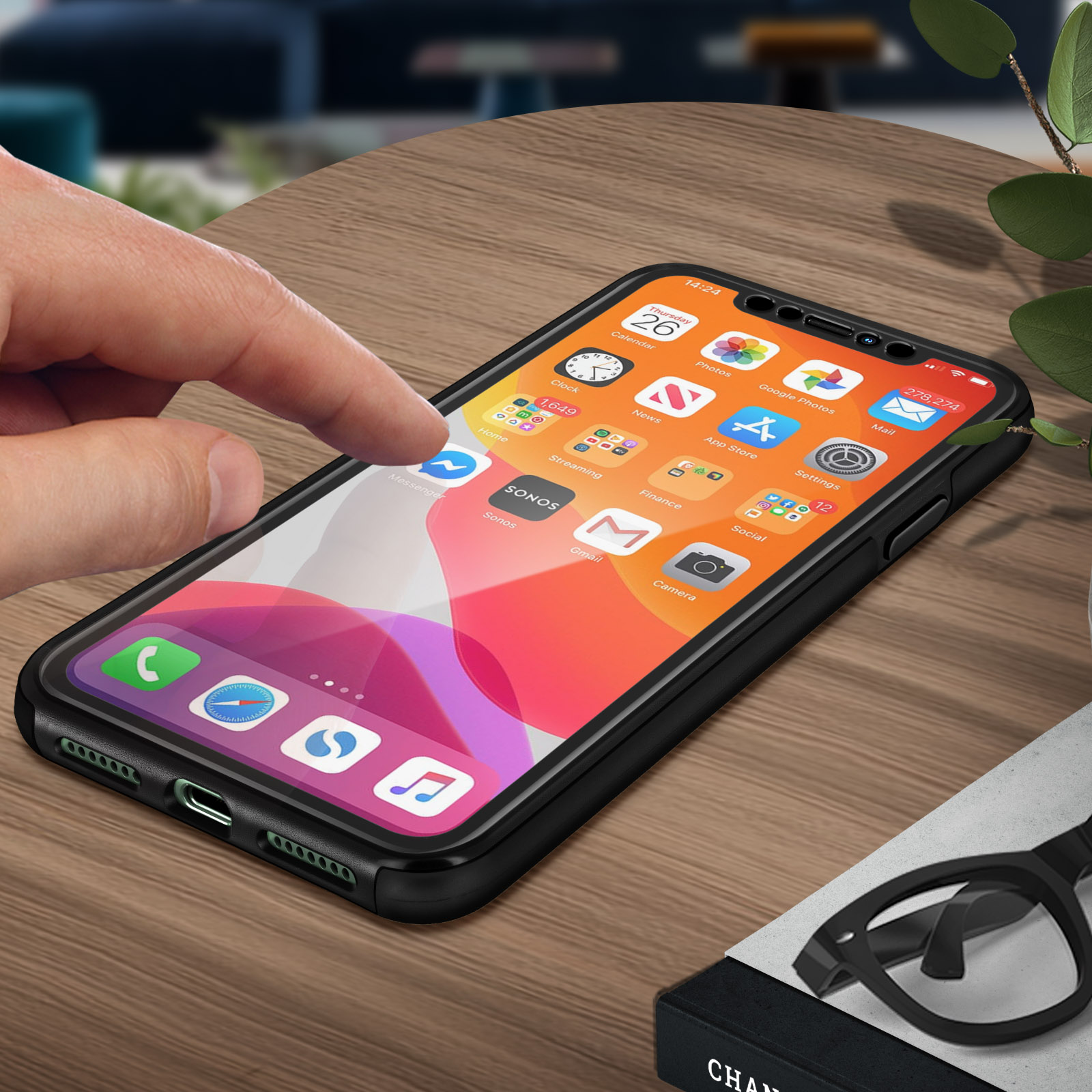 Main touchant l'écran d'un téléphone. Téléphone sur table en bois. Autres objets dans la scène.