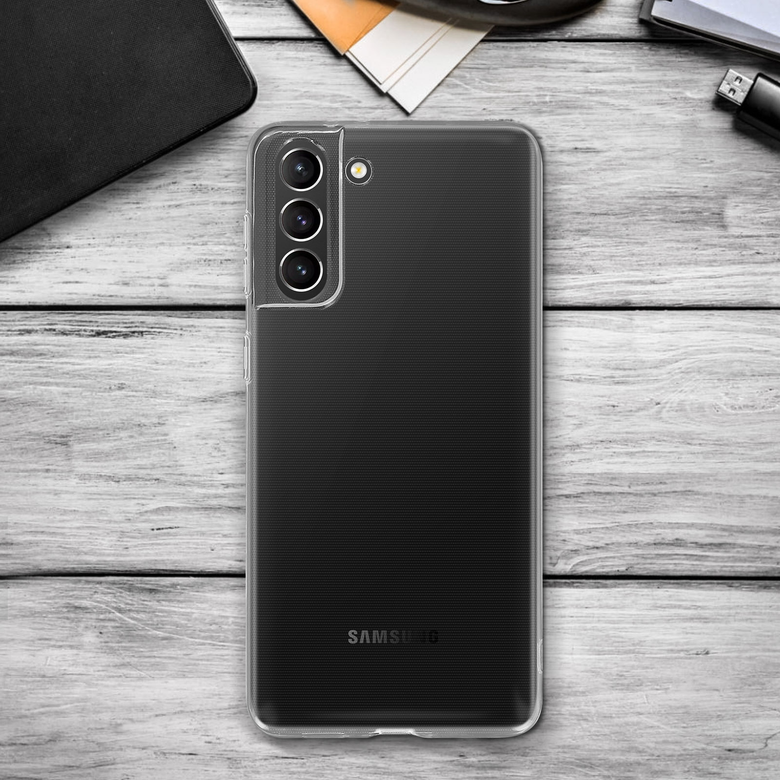 Telefono con custodia trasparente su una superficie di legno. Altri oggetti sullo sfondo.