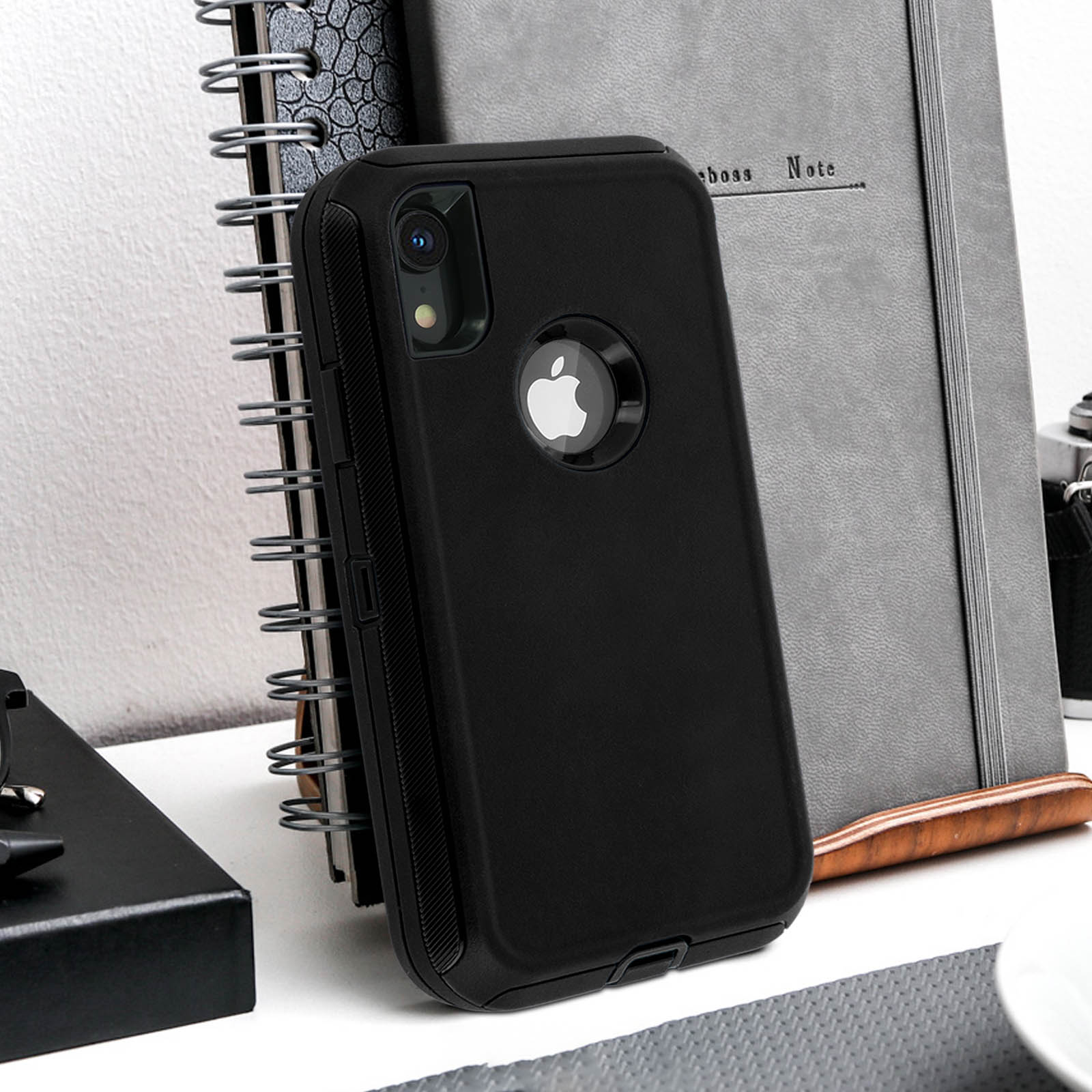 Una custodia nera per iPhone con il logo Apple. Un taccuino e un blocco note sullo sfondo.