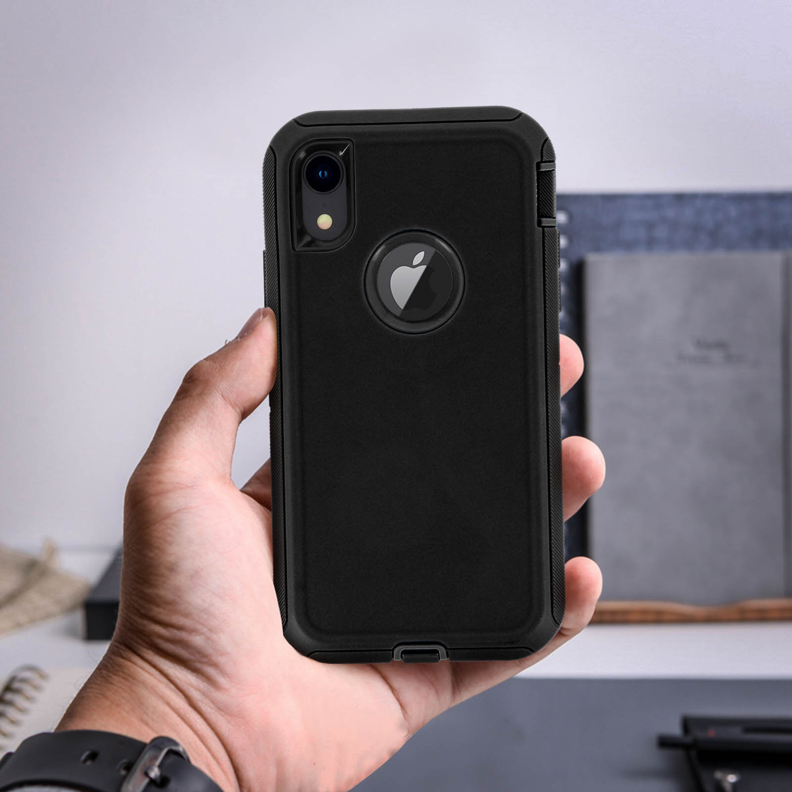 Una mano tiene un telefono nero in una custodia nera con il logo Apple visibile sul retro.