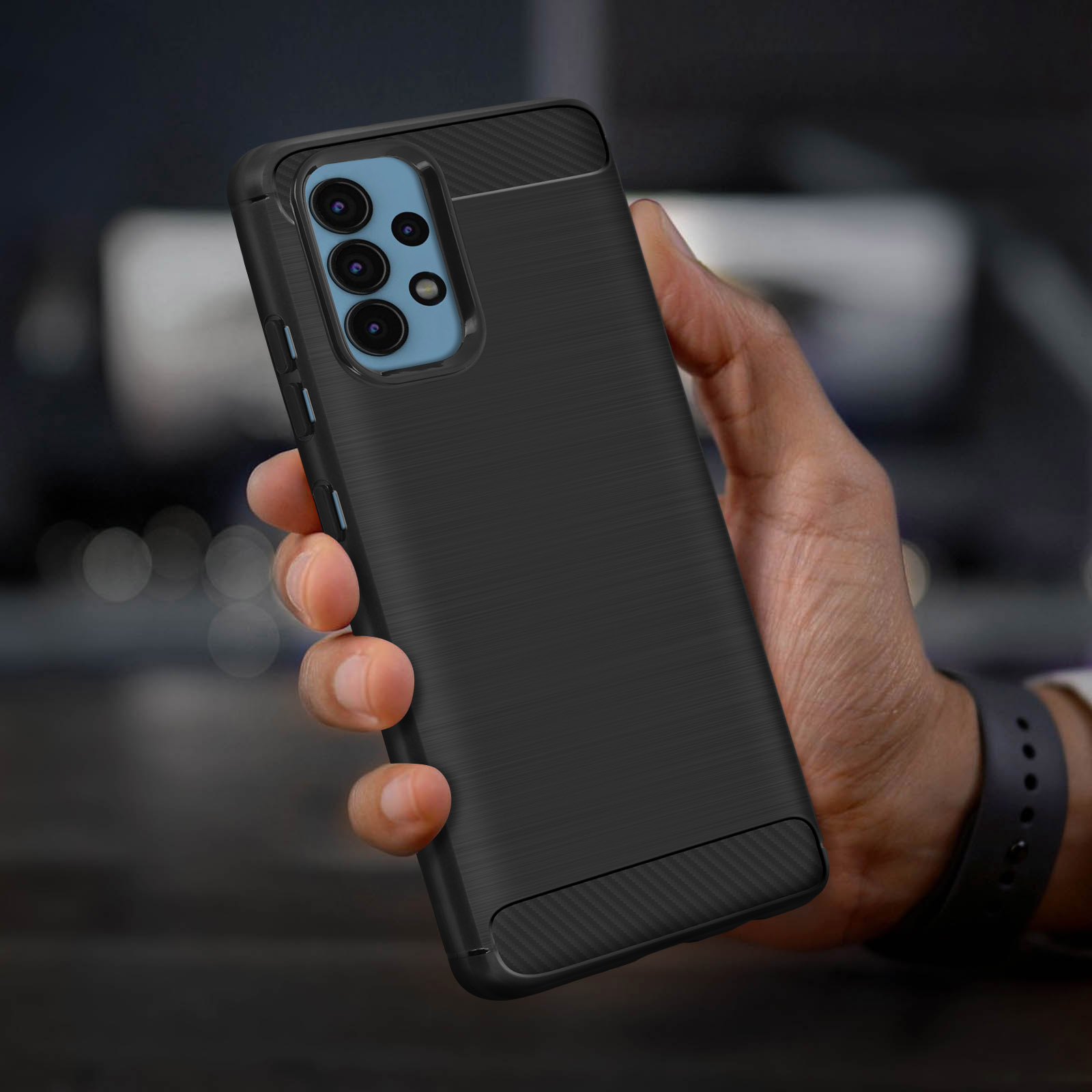 Una mano tiene un telefono nero con una custodia strutturata. Lo sfondo è sfocato.