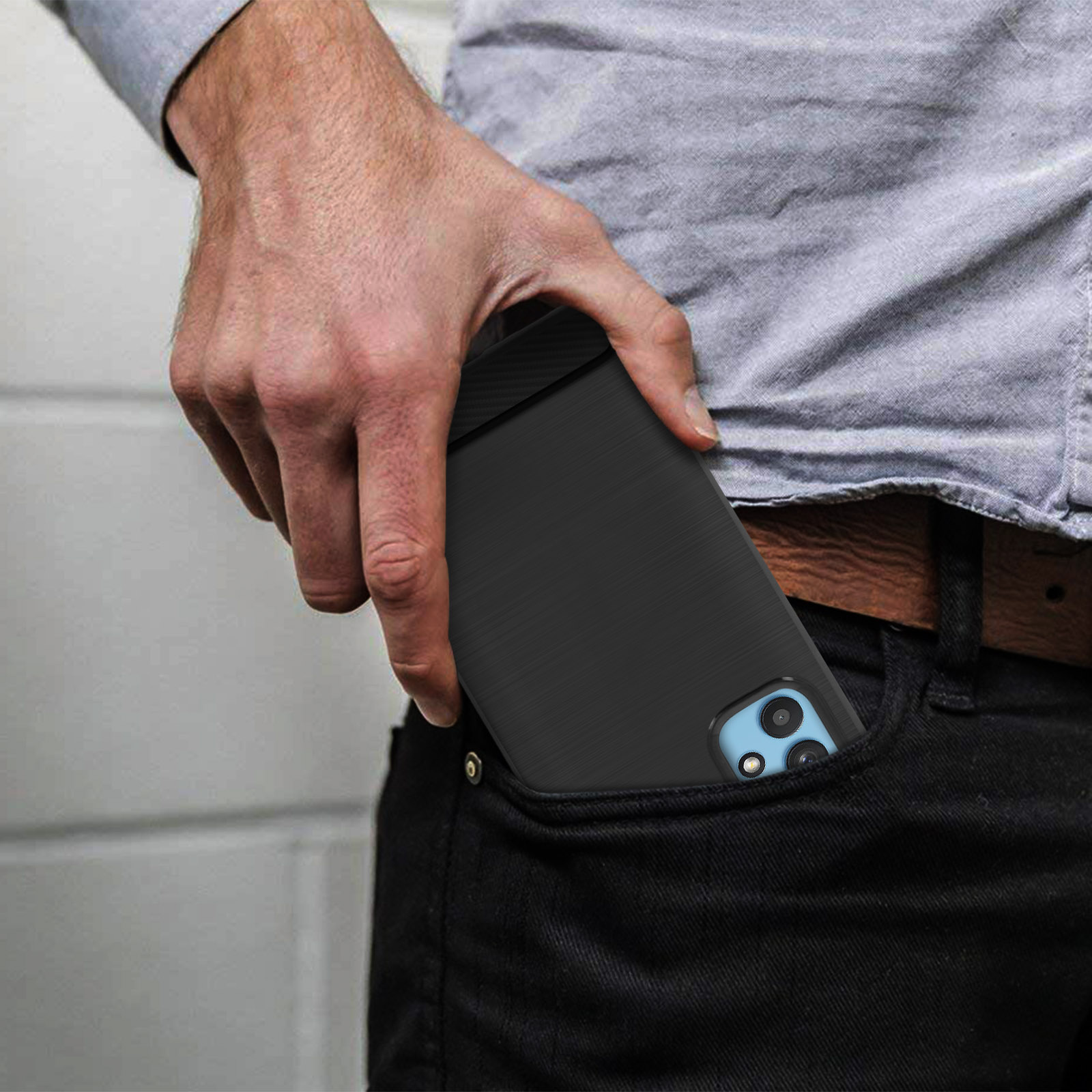 La mano di un uomo in tasca tiene un telefono nero. Il telefono ha una custodia nera. Parte della sua vita è visibile.