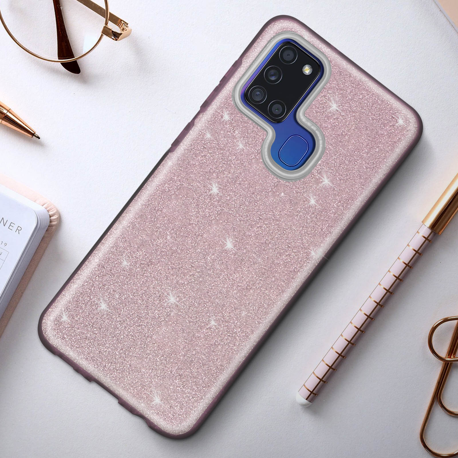 Roze glitter smartphonehoes. Het heeft een camera-uitsparing en ligt op een bureau met een pen en bril.