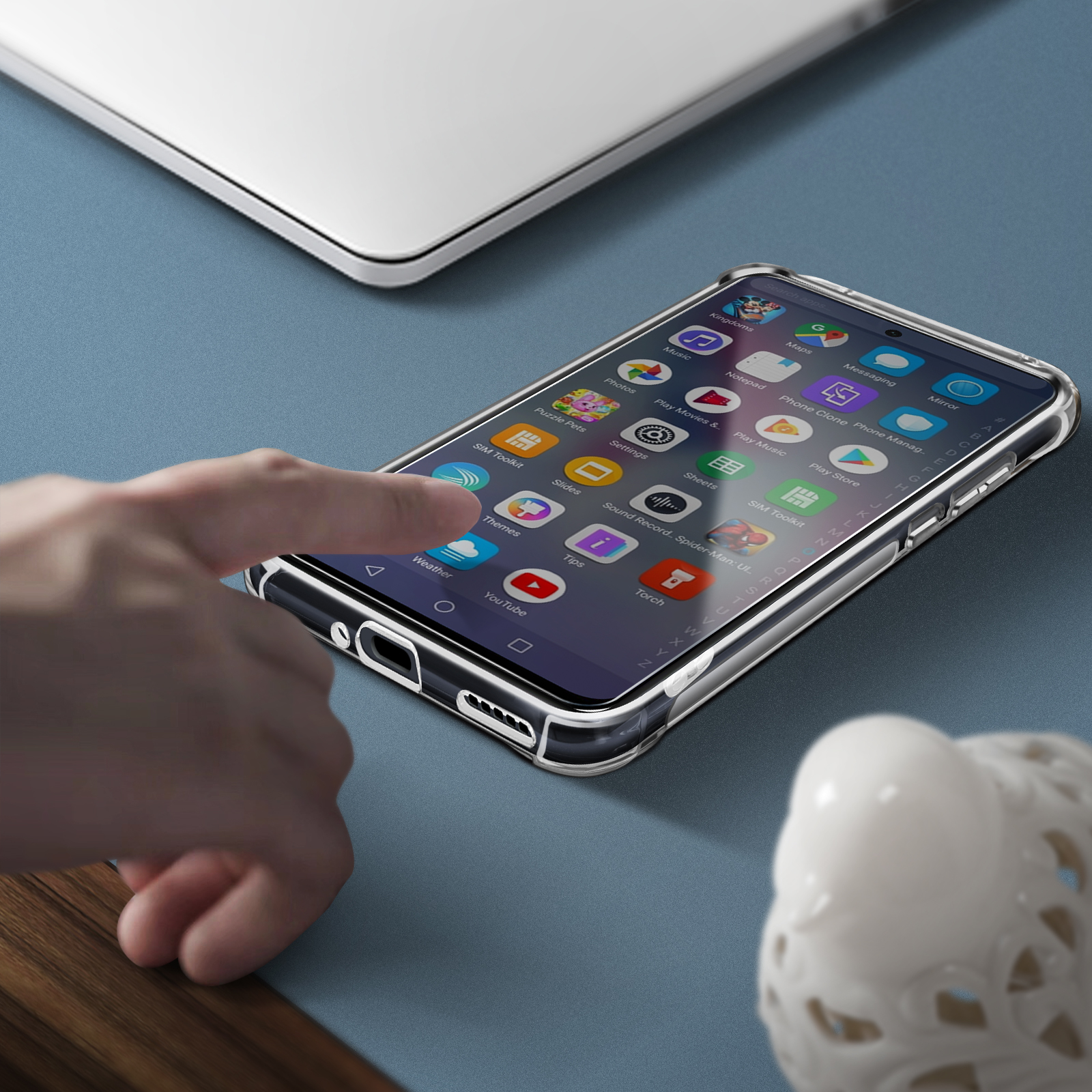 Telefono in custodia trasparente con icone di app su superficie blu. Una mano che afferra il telefono.