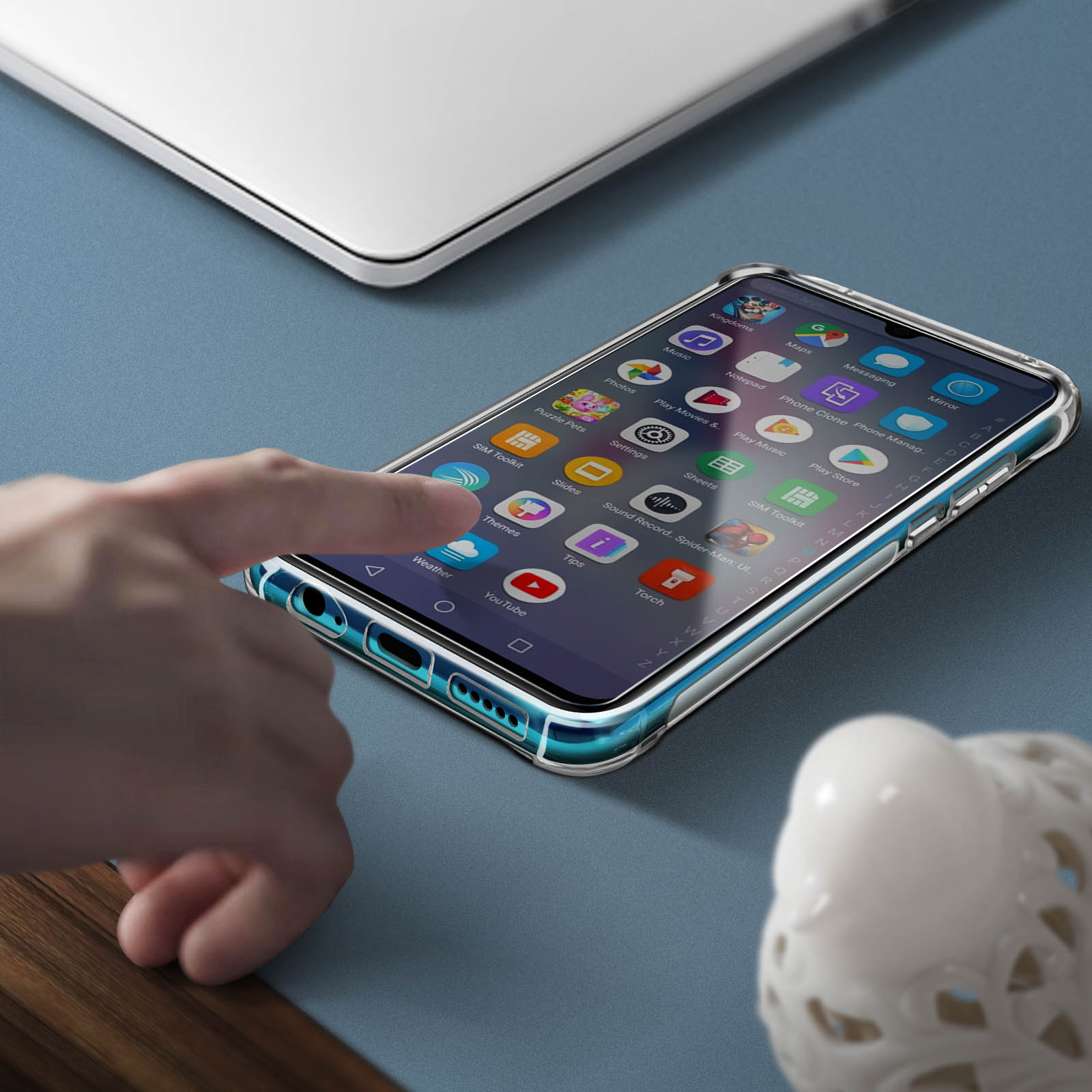 Mano tocca un telefono con app sullo schermo in una custodia trasparente. Un laptop sullo sfondo.