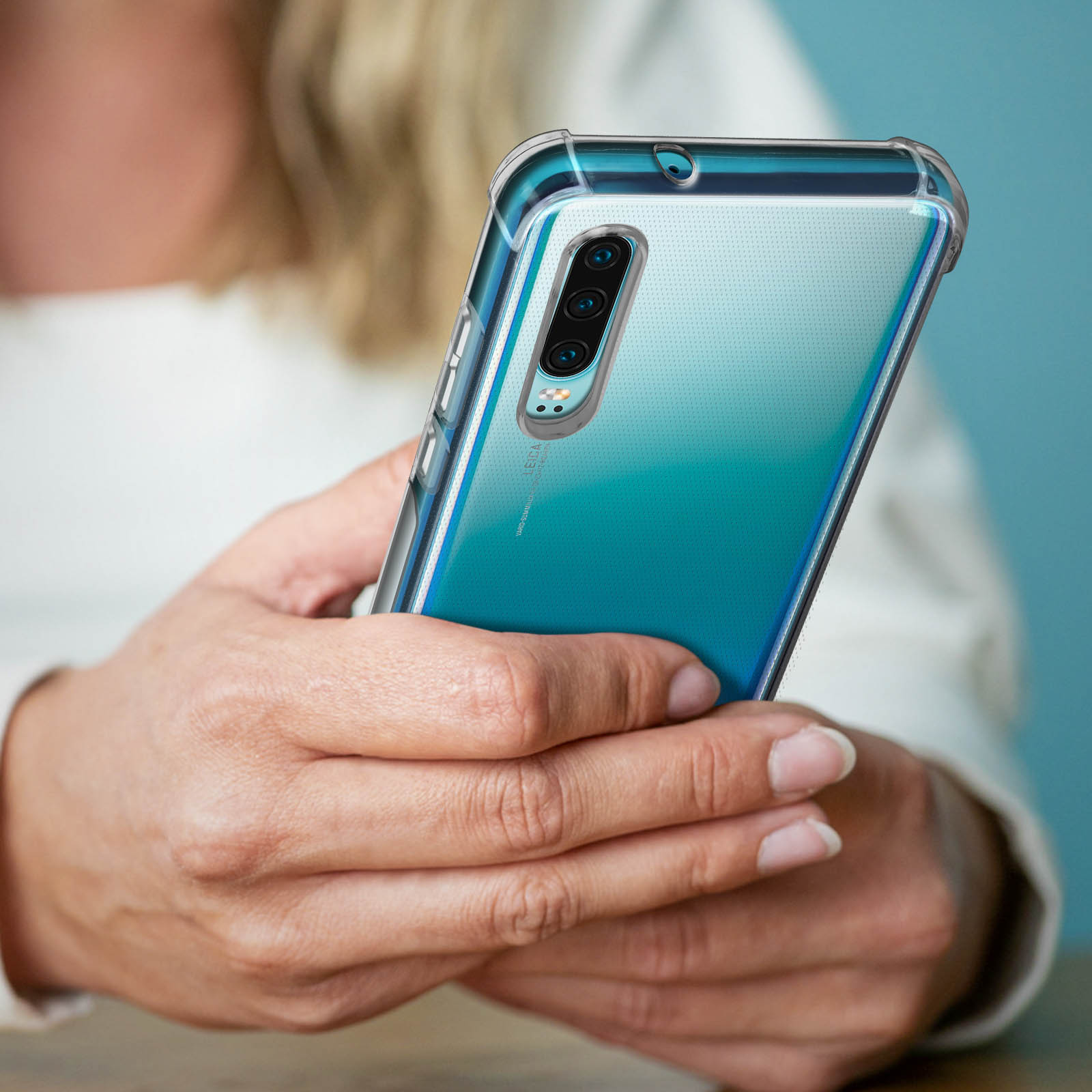Persona che tiene un telefono in una custodia trasparente, mostrando la fotocamera e il retro sfumato blu-verde.