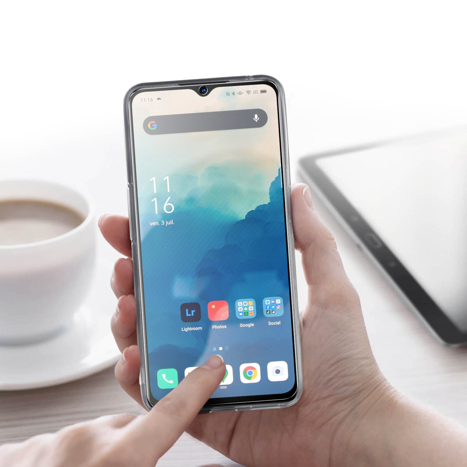 Una mano che tiene un telefono con app visualizzate sullo schermo. Sono visibili una tazza e un tablet.